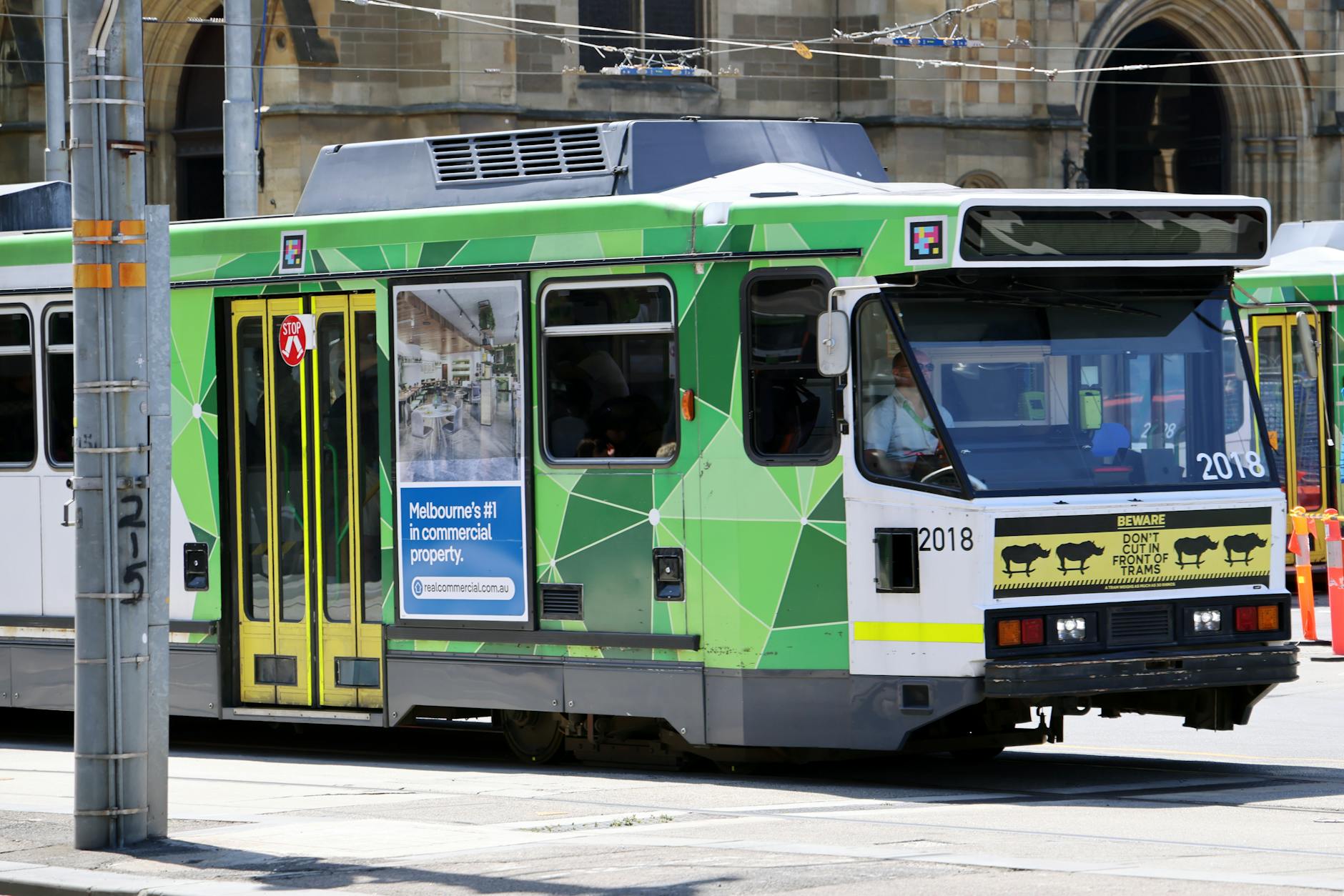 Green Melbourne tram moving through city streets.