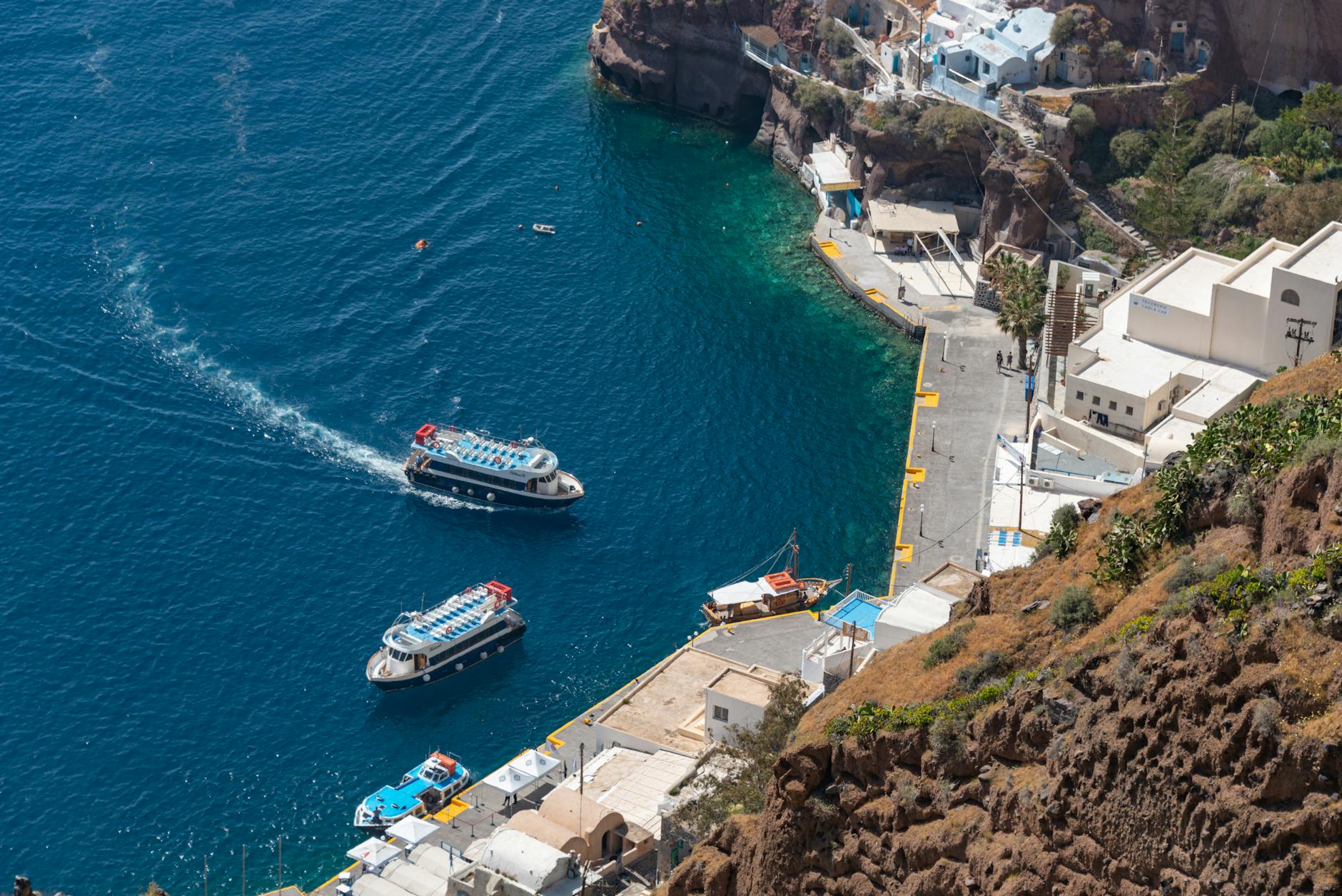 Old harbor and boats below Santorini cliffs.