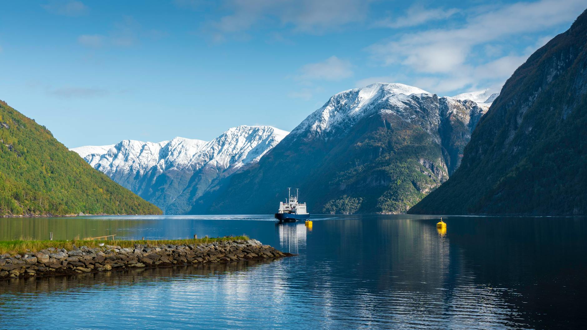 Ferry crossing a Norwegian fjord surrounded by snowy mountains.