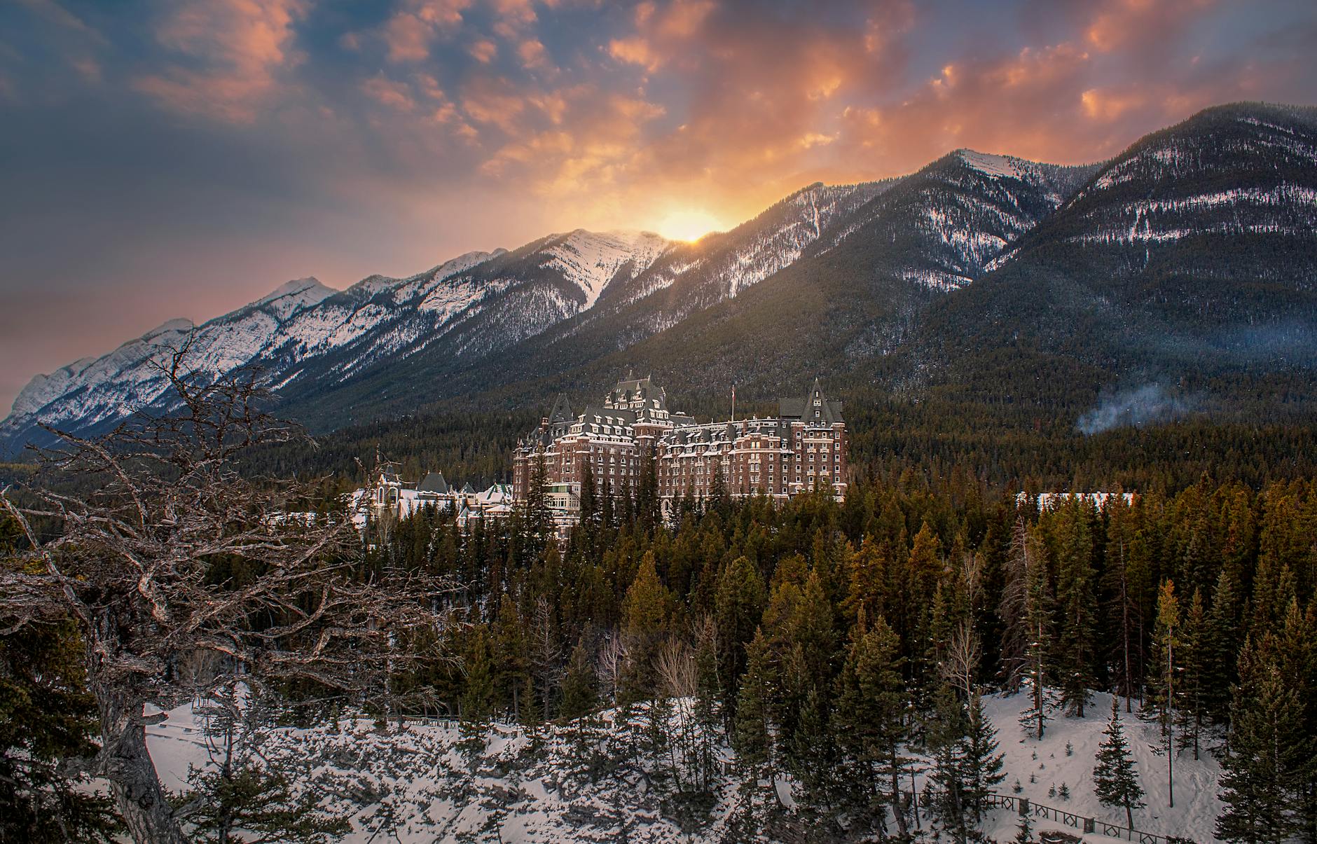 Scenic view of Banff Springs Hotel amid snow-covered mountains at sunset.