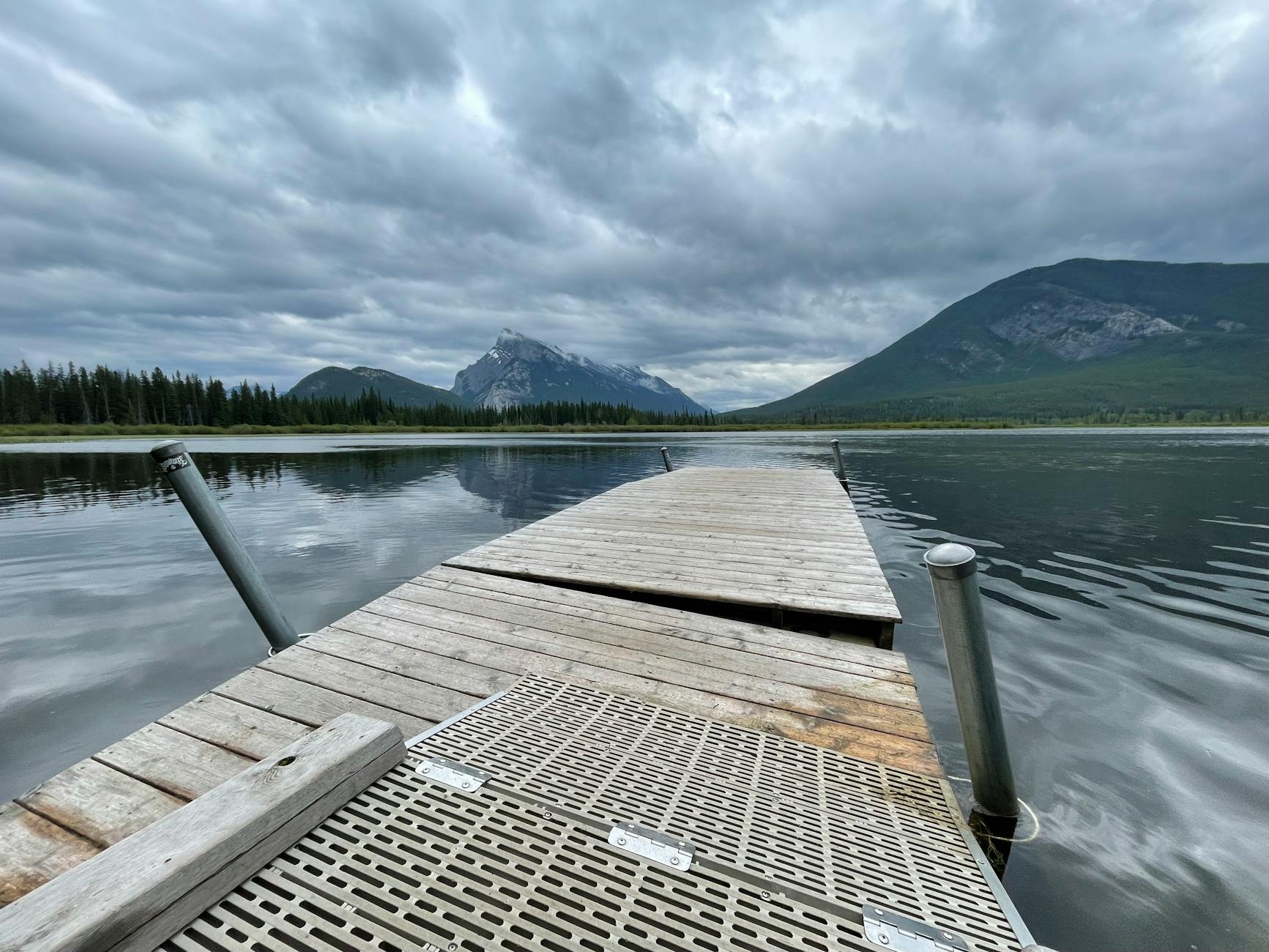 Peaceful wooden dock extending into a serene mountain lake under cloudy skies.