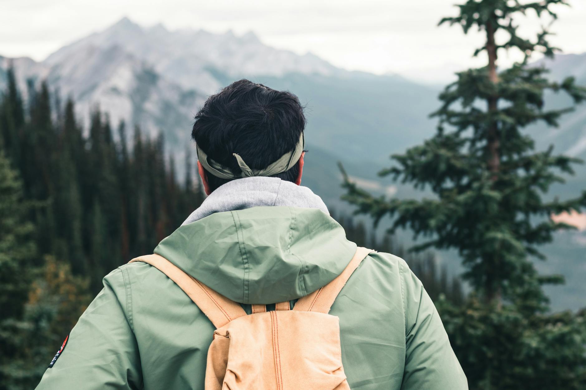 Back view of a hiker in a green jacket exploring mountainous wilderness of Canada.