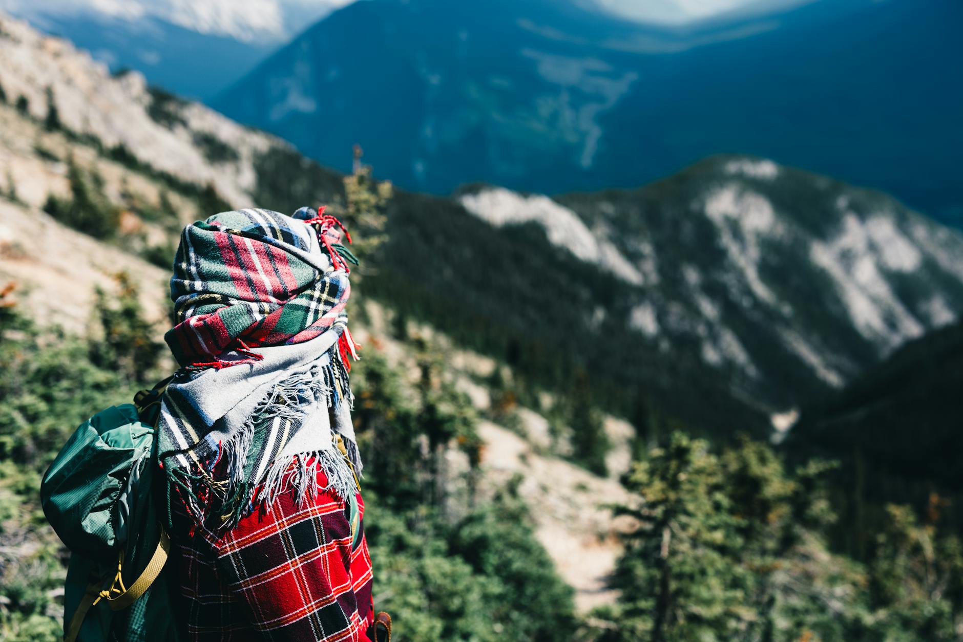 A hiker wrapped in a plaid scarf enjoys a panoramic view of Banff National Park, Canada.