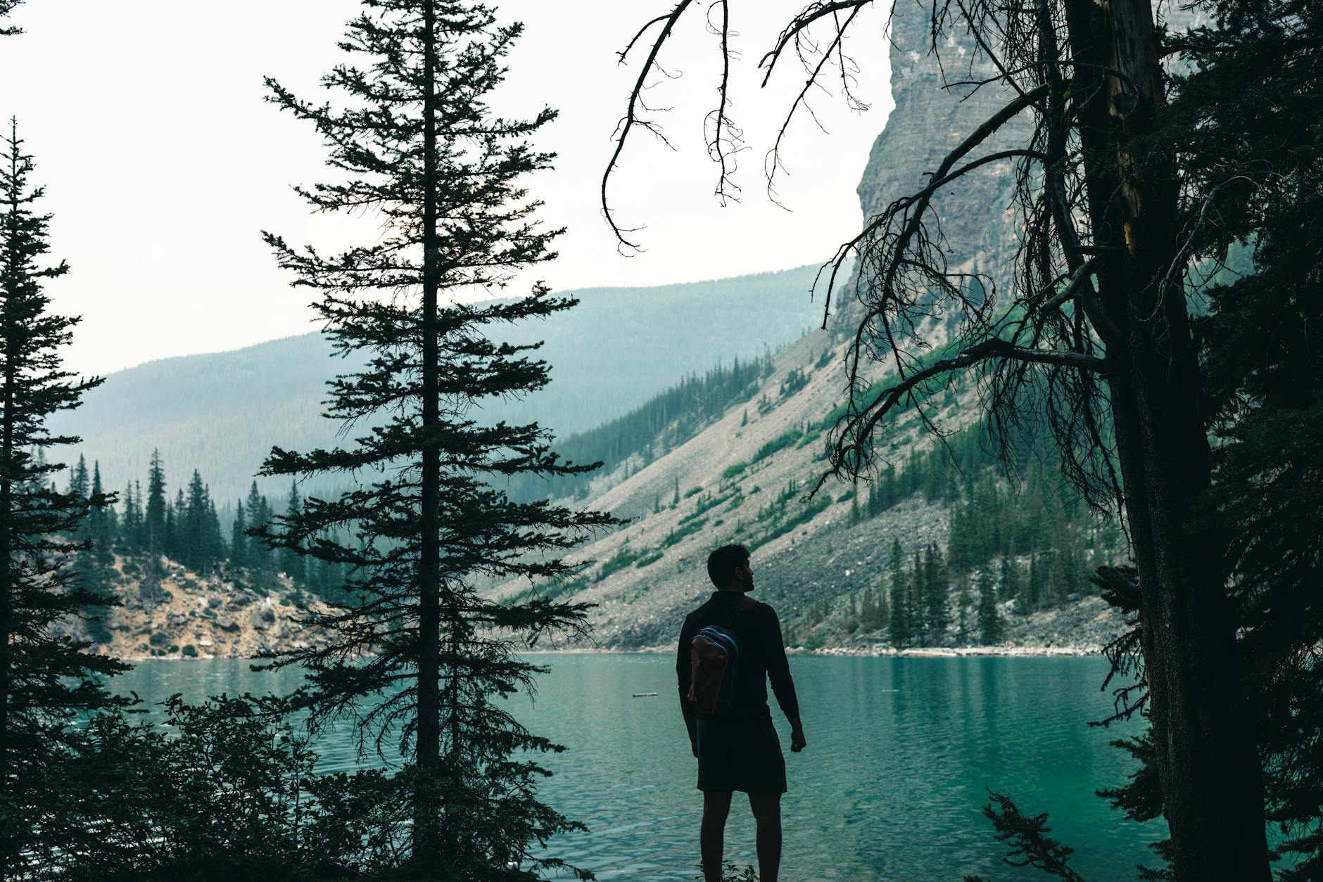 Silhouette of a man by a turquoise lake in Banff surrounded by coniferous trees and mountains.
