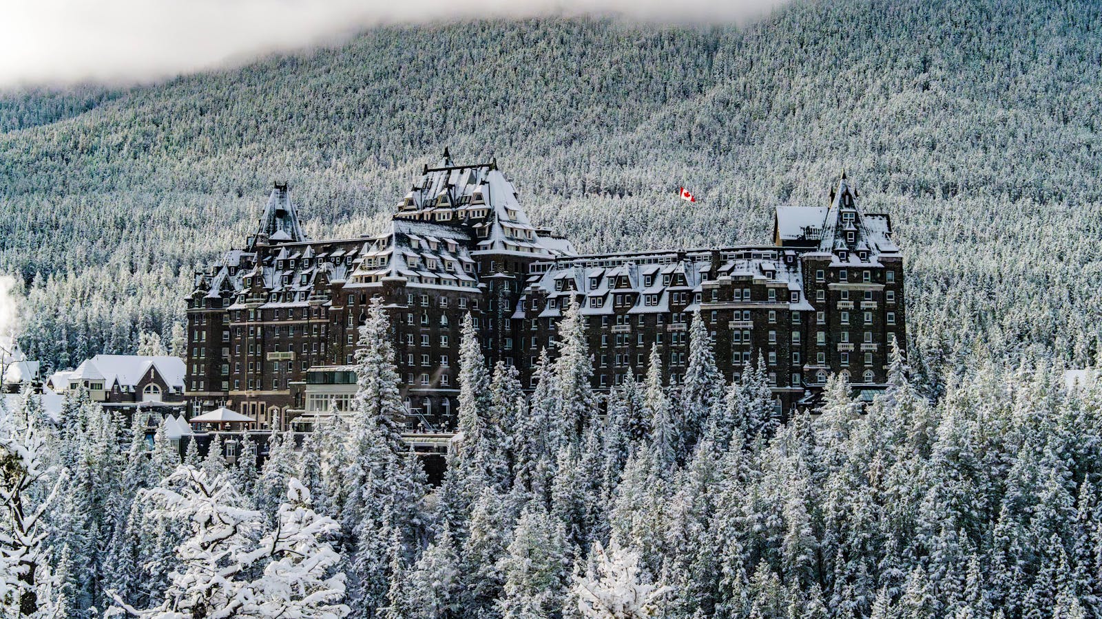 Winter view of Banff Springs Hotel surrounded by snowy forests and mountains.