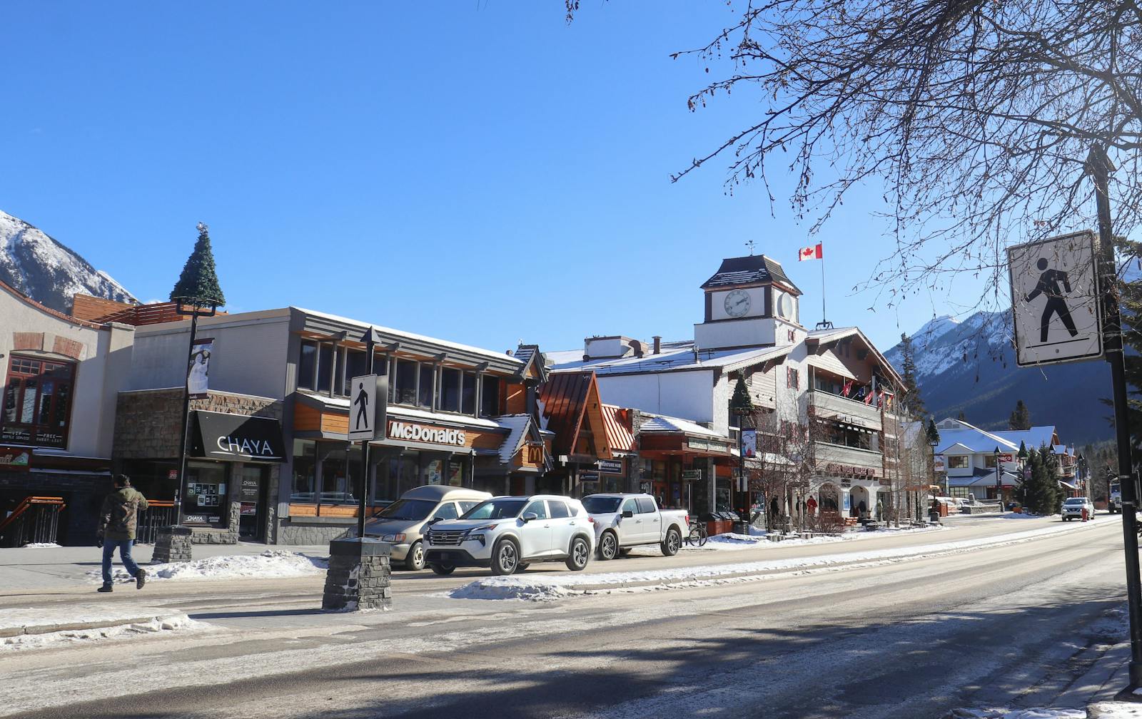 Winter day on Banff Avenue with snowy streets, shops, and mountains.