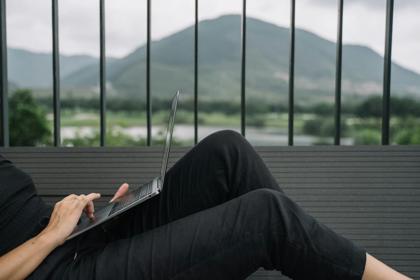 Person working remotely on a laptop with a serene mountain view from a balcony.