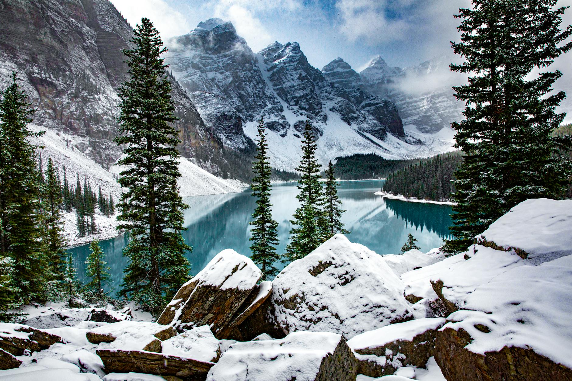Majestic winter landscape of Moraine Lake surrounded by snow-covered mountains and pine trees.