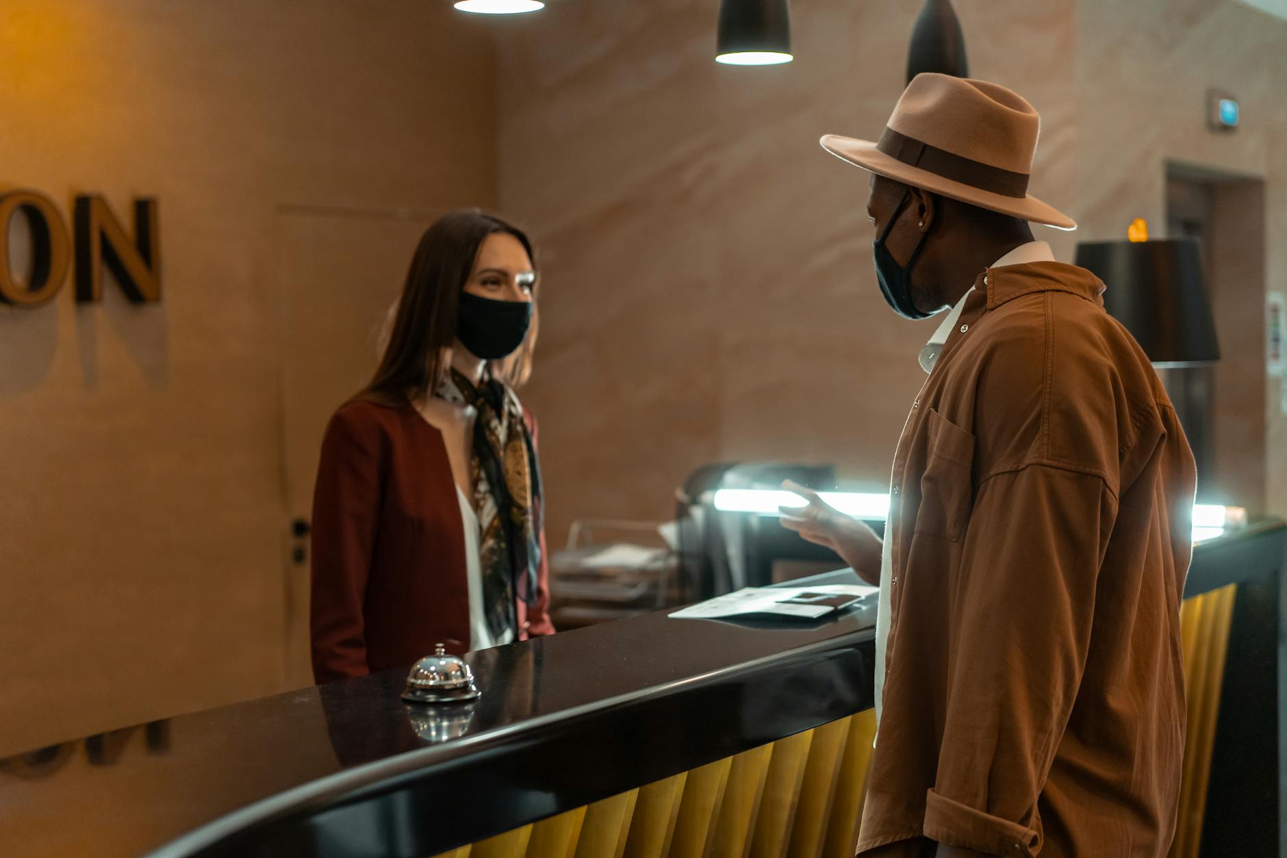 A man at a hotel reception talking to a staff member. Both wear face masks.