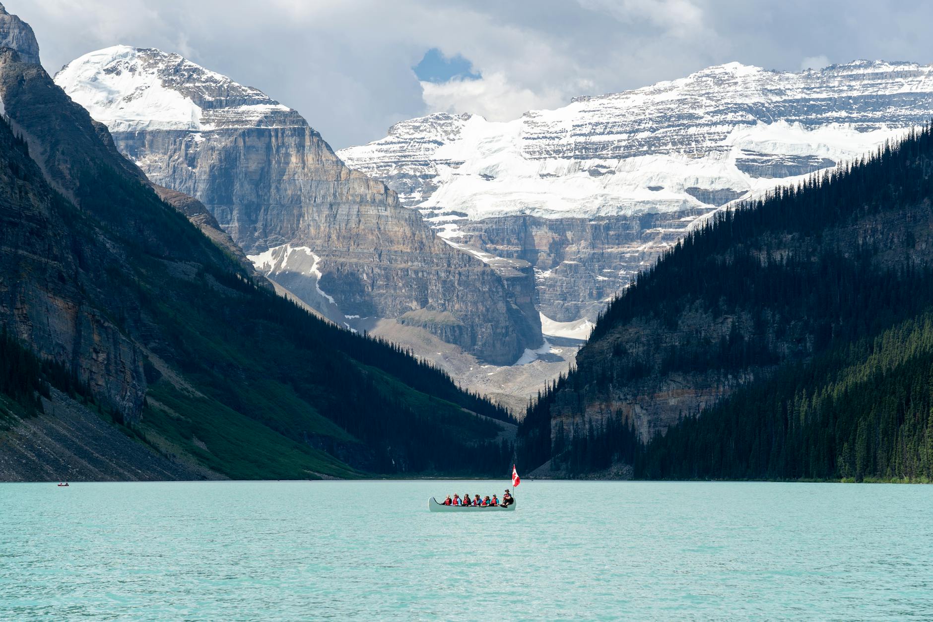 A group enjoys a canoe ride on turquoise Lake Louise with majestic snow-capped mountains in the background.
