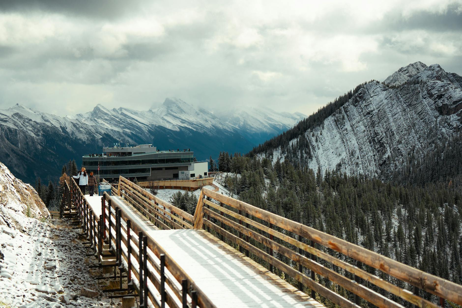 Winter mountain landscape with a snowy wooden path leading to a modern building.