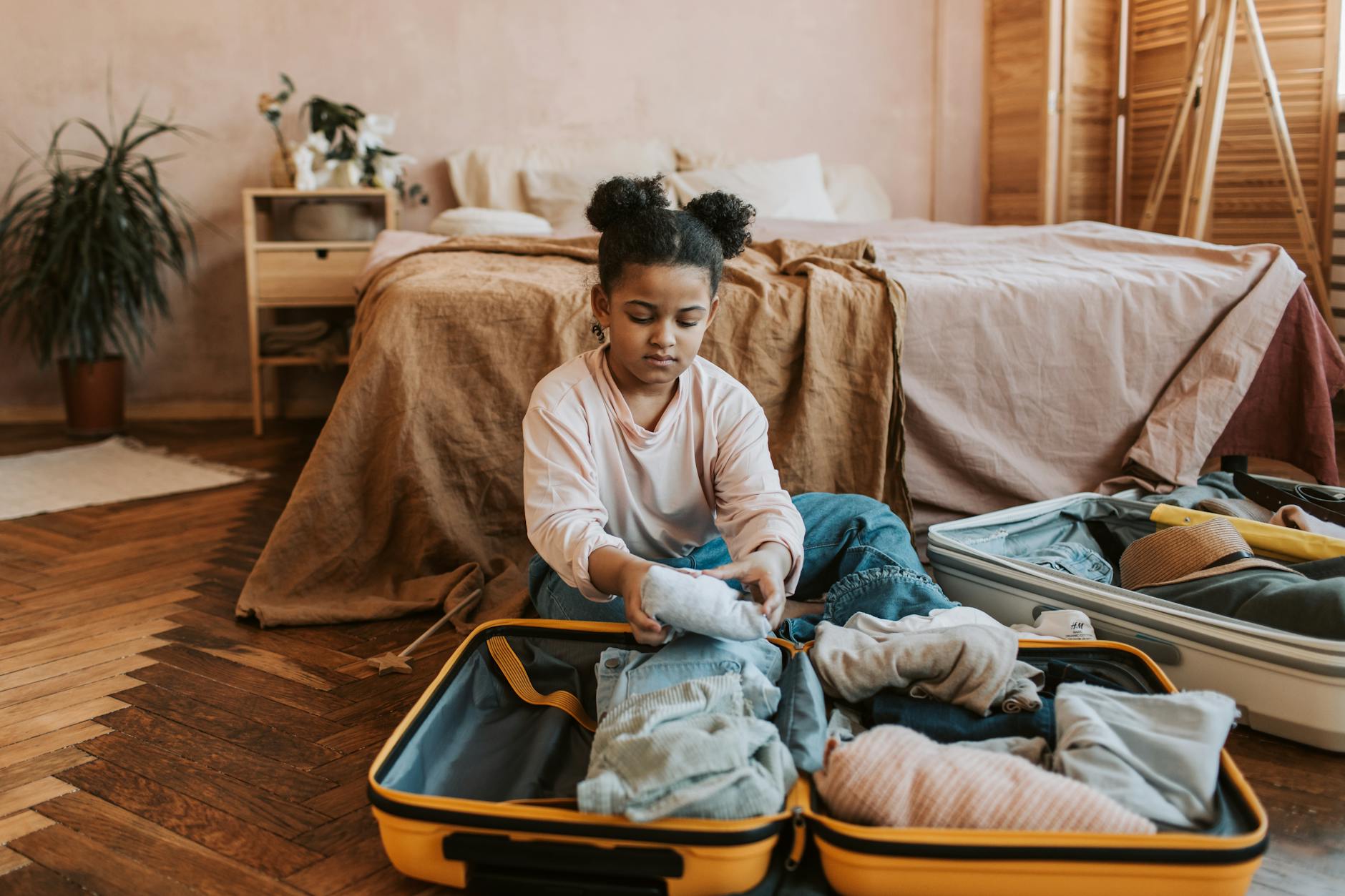 A young girl folding clothes into a suitcase in a cozy bedroom setting with natural decor.