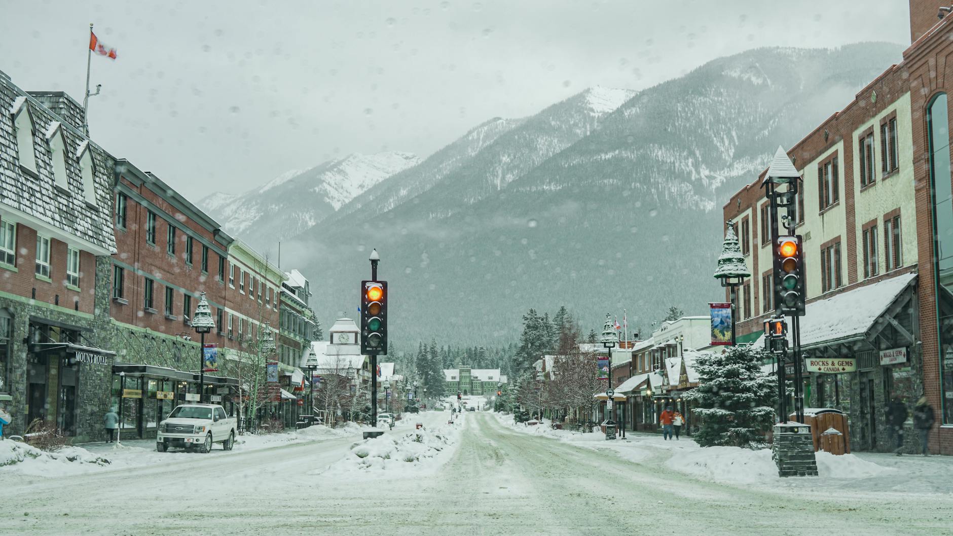 Snow-covered street in Banff, Alberta with mountain backdrop and stoplights