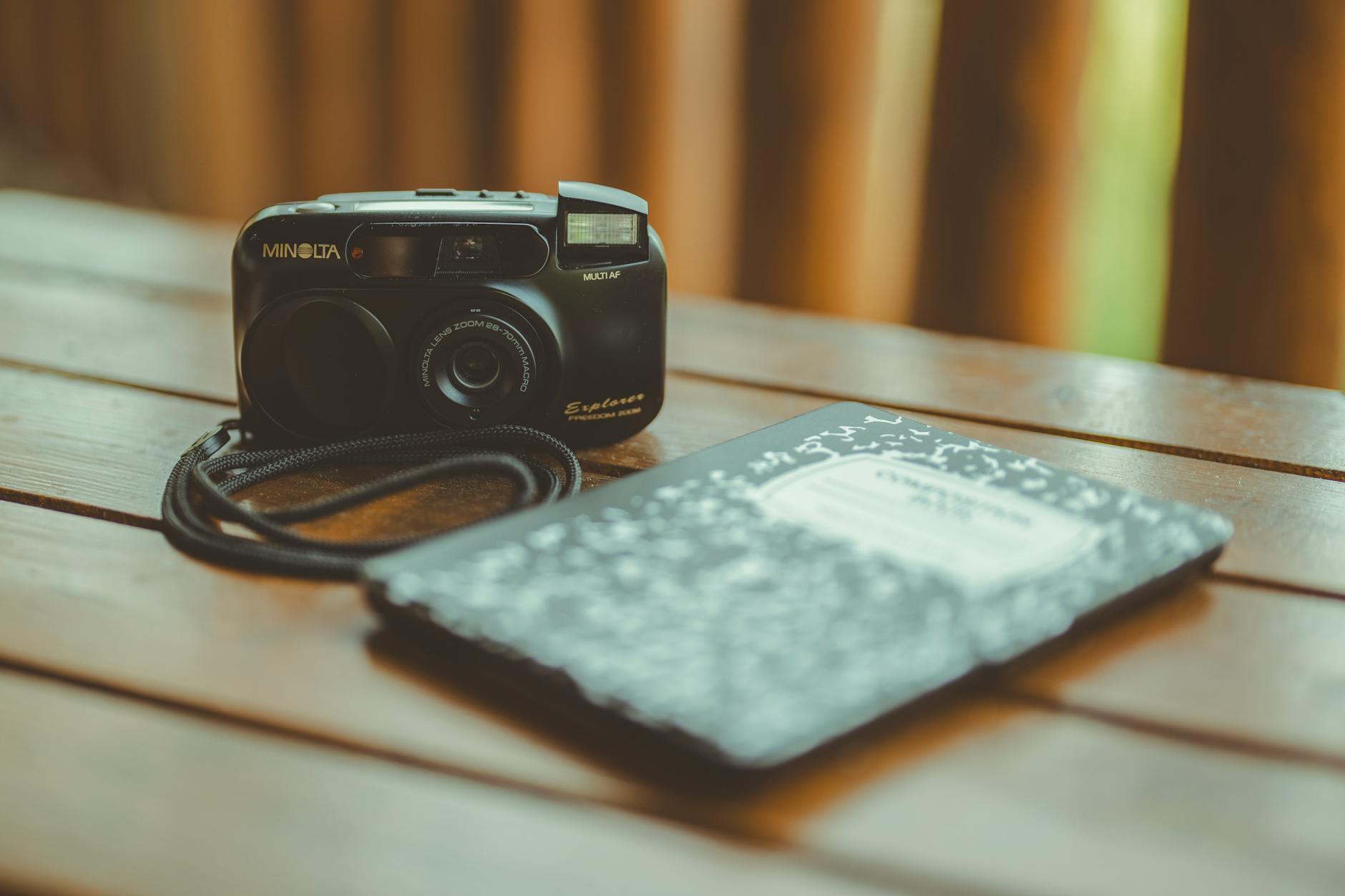 A vintage Minolta camera and a notebook rest on a wooden table, capturing a nostalgic analog vibe.