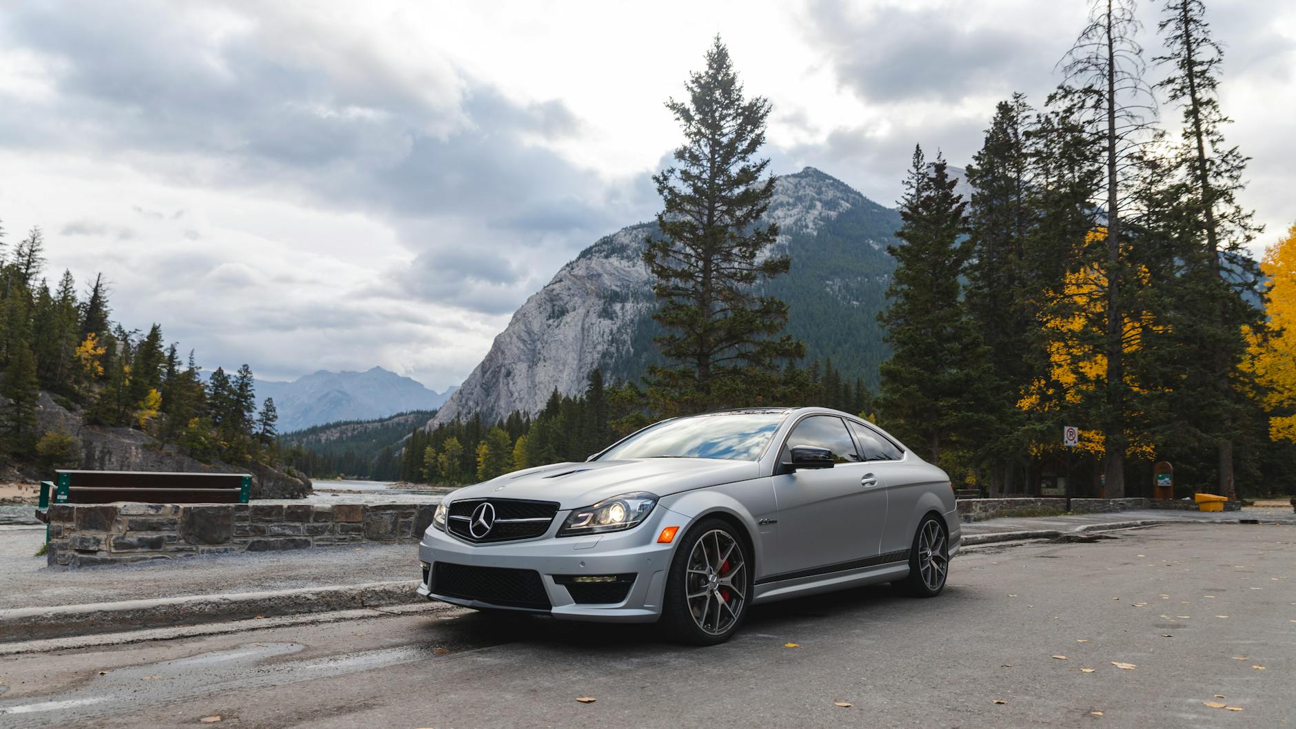 A silver luxury sports car parked on a serene mountain road with stunning natural scenery.