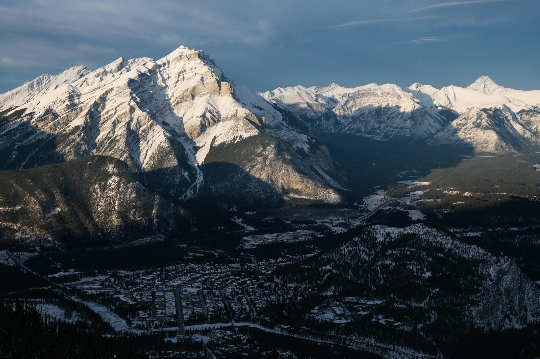 Majestic snowy peaks overlooking a serene valley town under clear winter skies.