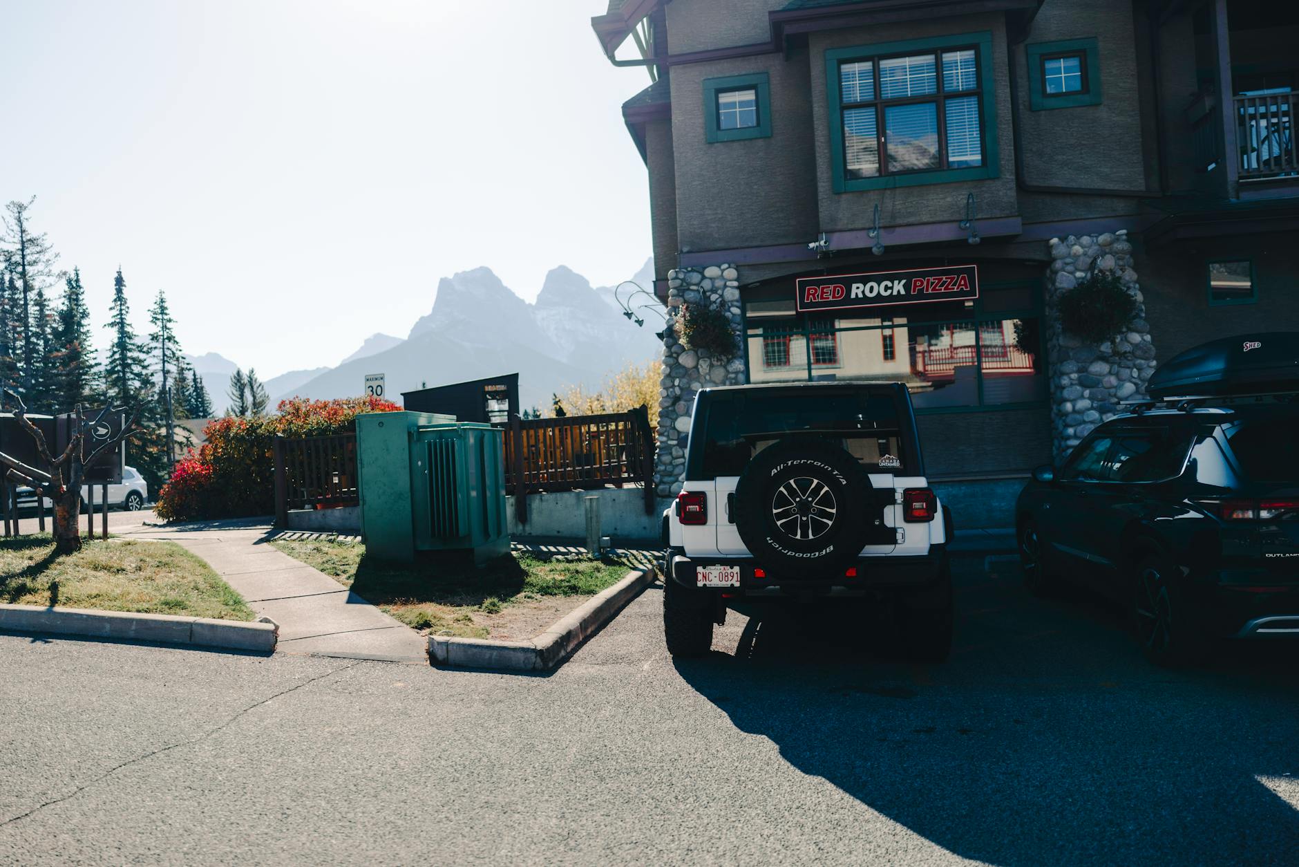 Parked cars near Red Rock Pizza with mountain backdrop in Canadian Rockies.