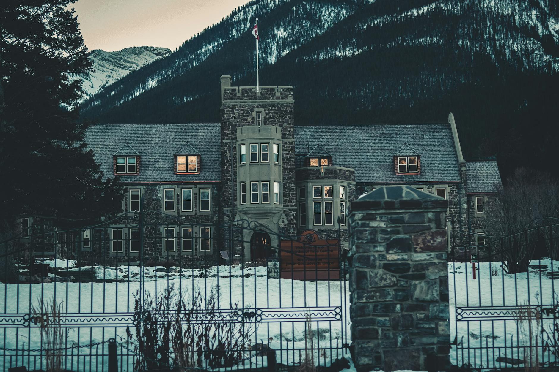 A historic stone building nestled in the snowy landscape of Banff, Alberta, framed by mountains.