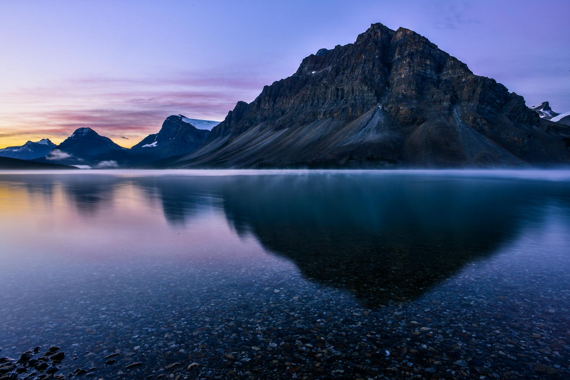 Serene sunrise over calm lake reflecting rugged mountains in Banff National Park.