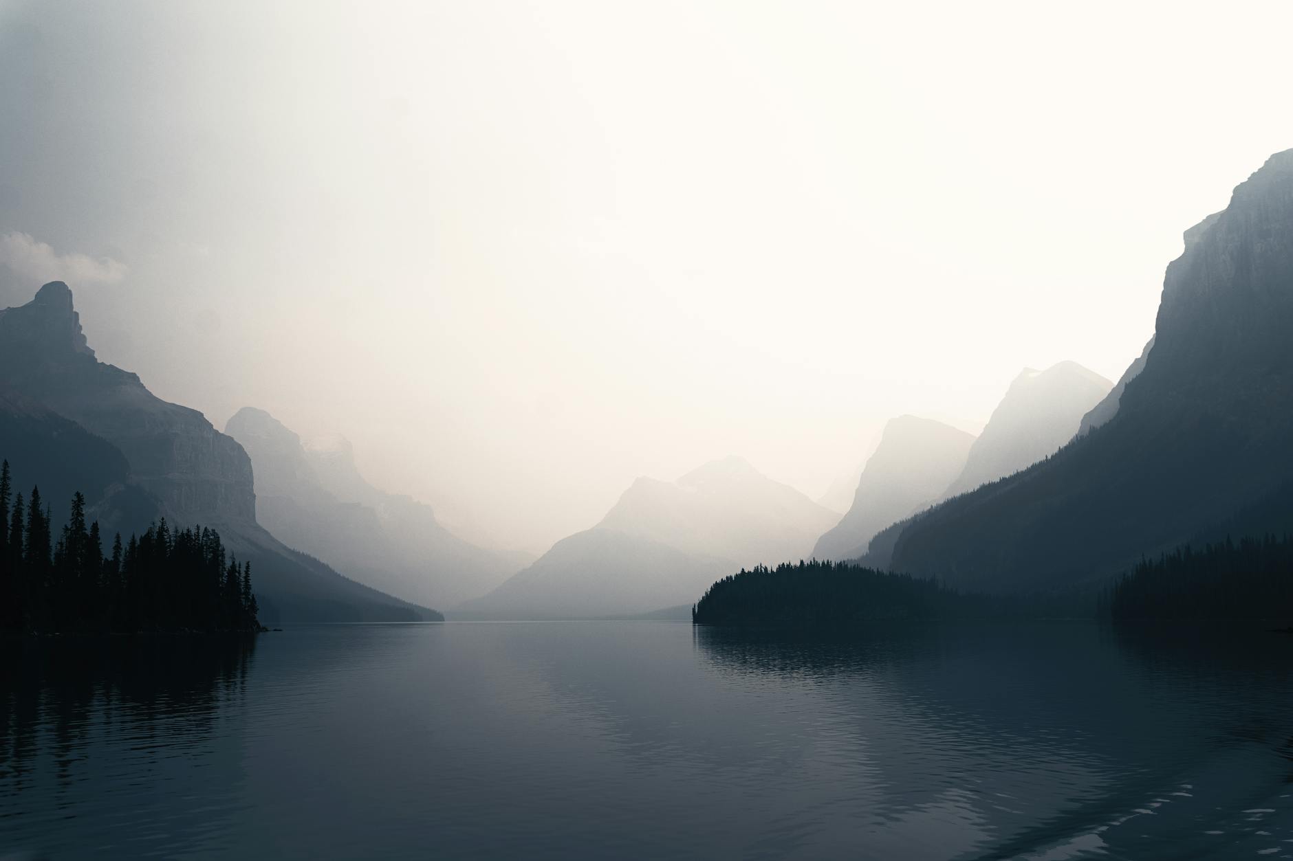 Misty morning view of a tranquil lake surrounded by mountains in Banff, Canada.