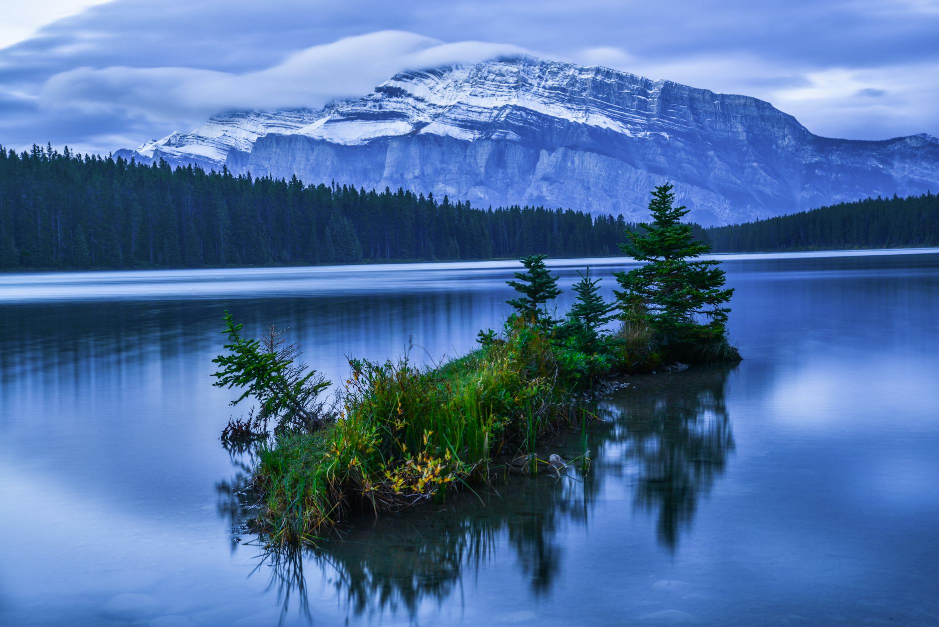 Calm lake reflecting snow-capped mountains in Banff at twilight, Canada.