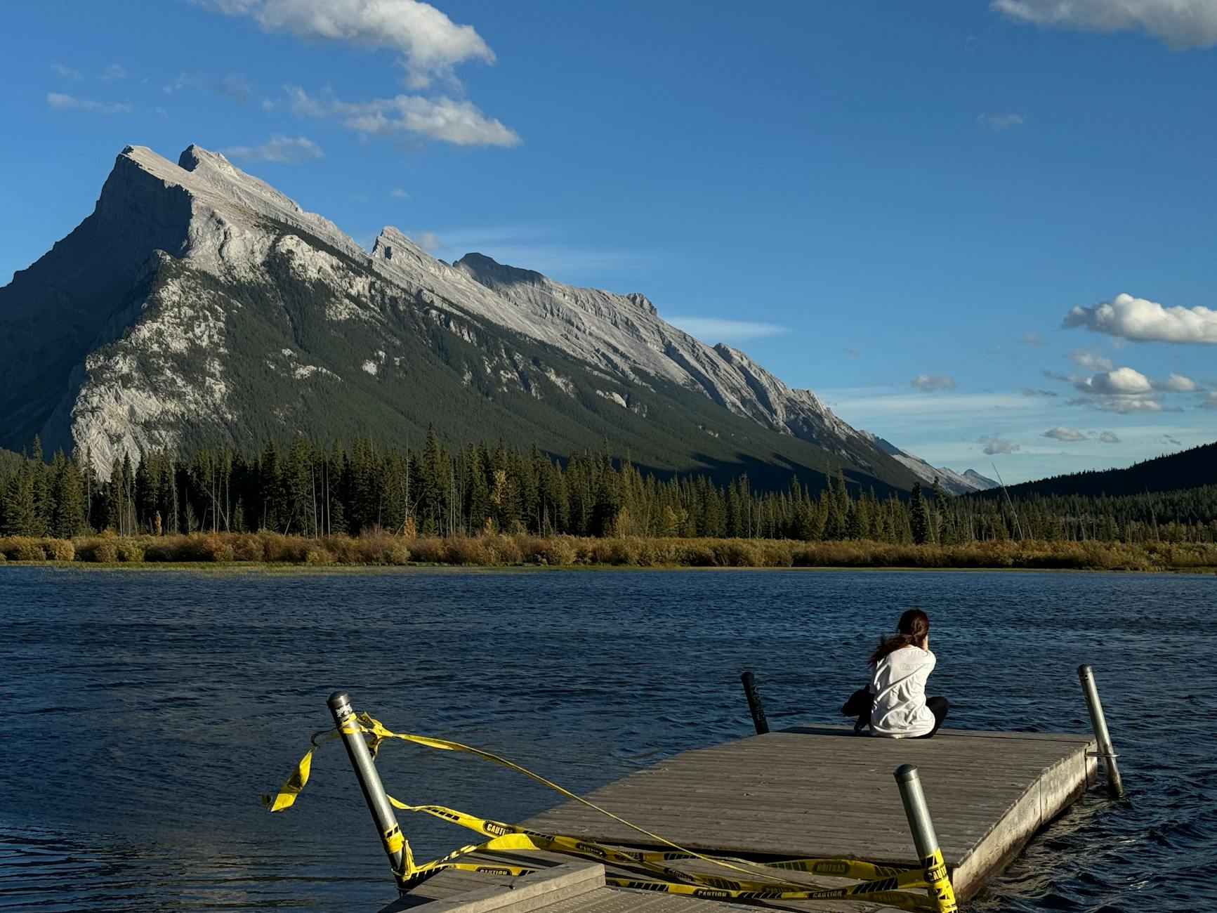 Woman sitting on dock with scenic mountain view at Vermilion Lakes, Banff, Canada.