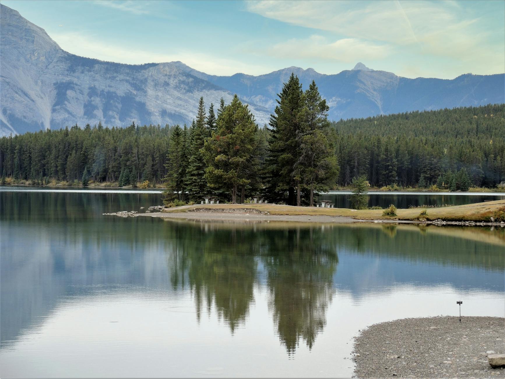 Peaceful mountain lake with conifer reflection in Alberta, Canada. Calm and picturesque spring scene.