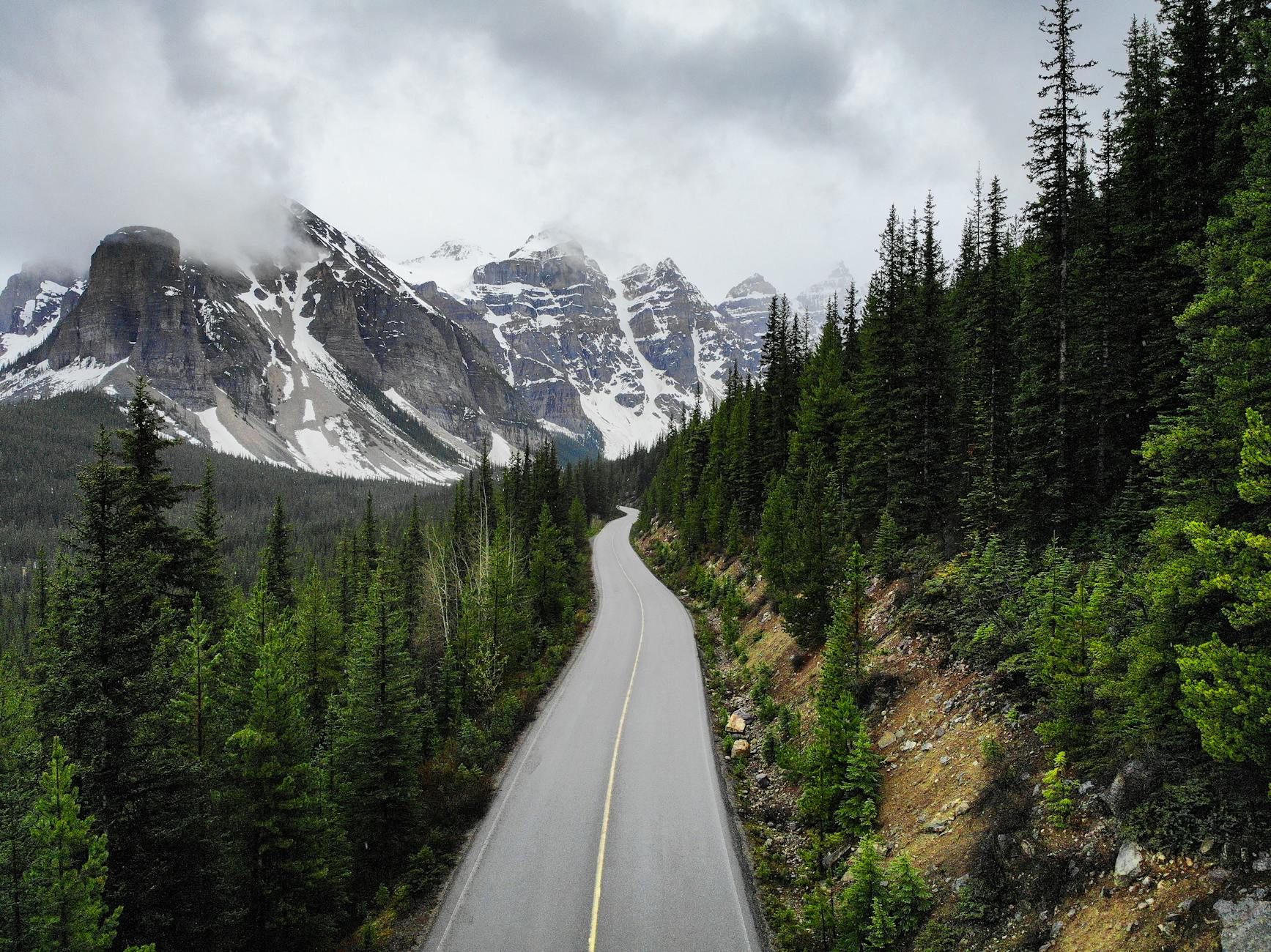 A winding road through Banff National Park with snow-capped mountains and dense forests.