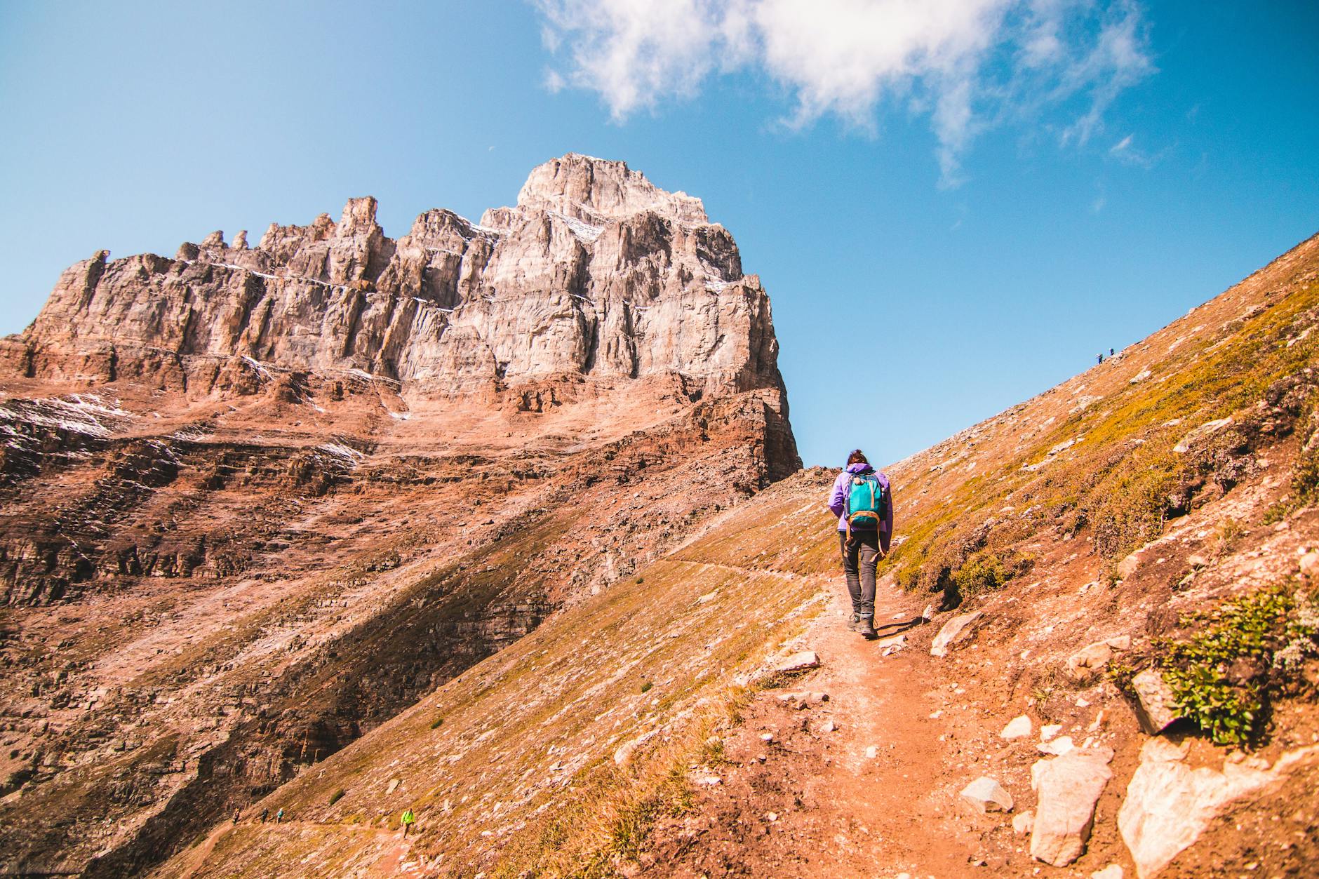Person hiking towards dramatic rock formations in Banff, Canada, under a clear blue sky.