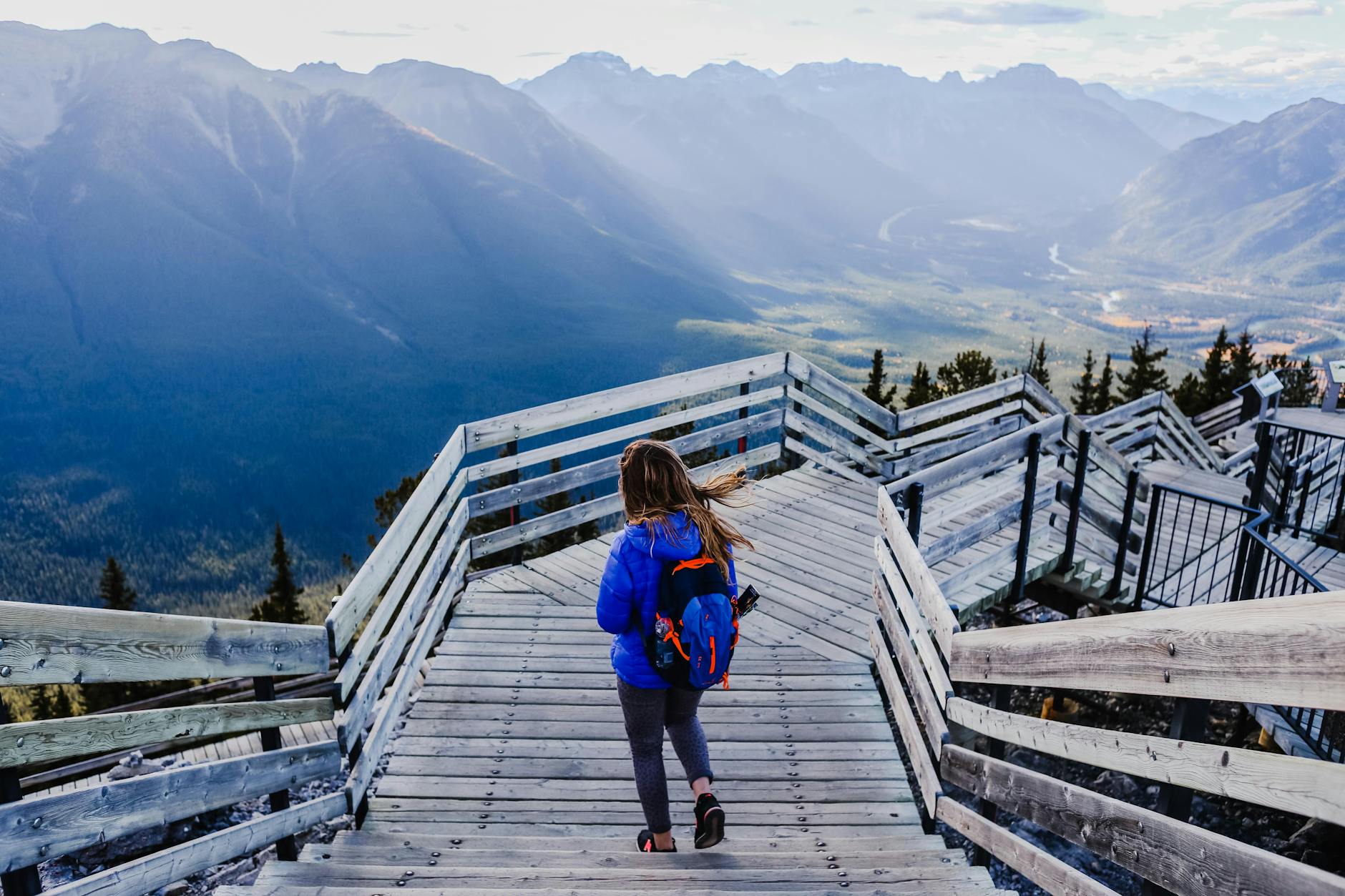 A woman descends a scenic wooden staircase in the mountains, offering breathtaking views.