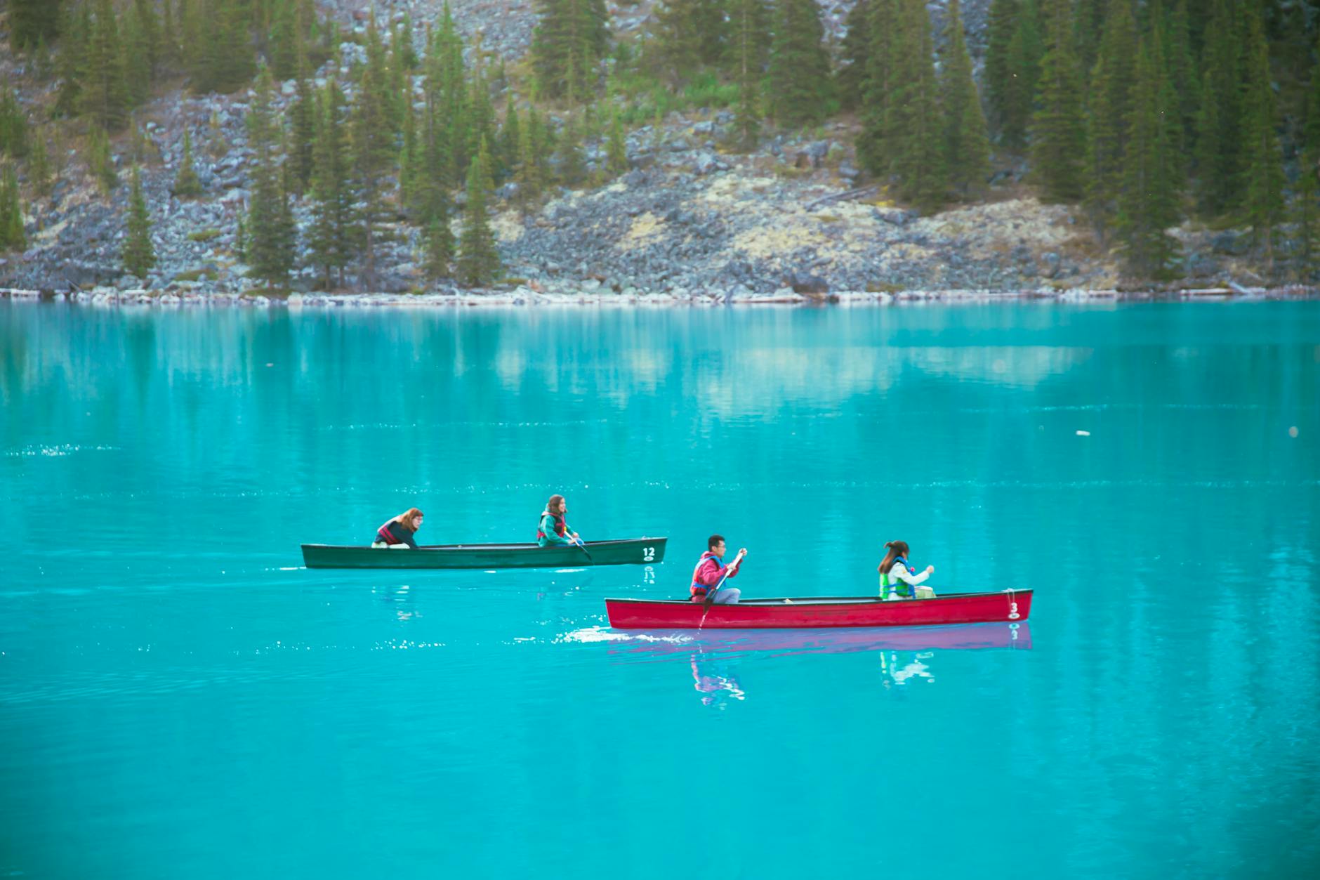 Tourists floating in boats over calm azure lake surrounded by mountains and forest