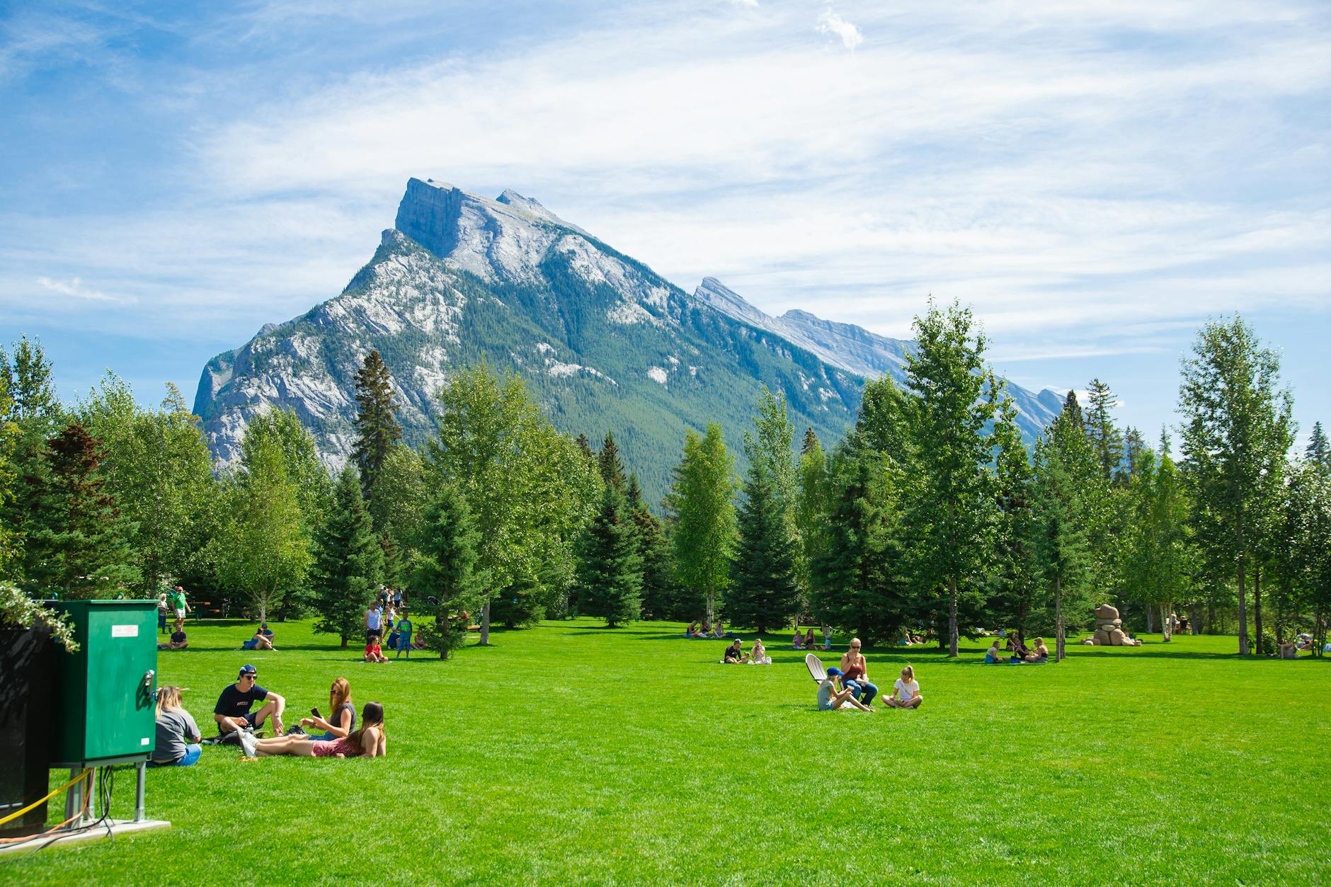People sitting on green grass against rocky mountains under cloudy blue sky in daytime