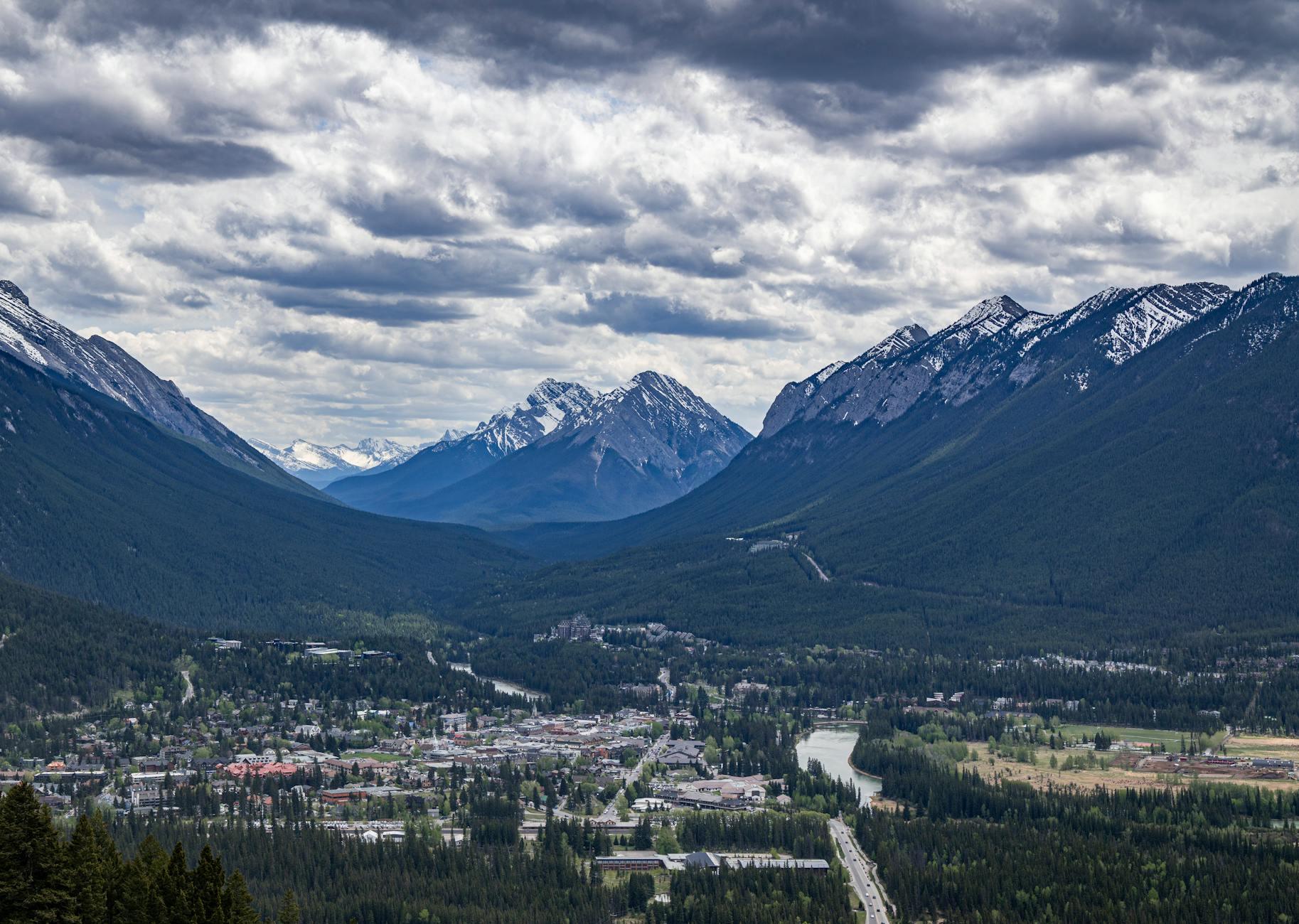 A breathtaking view of Banff town surrounded by mountain ranges under a dramatic cloudy sky.