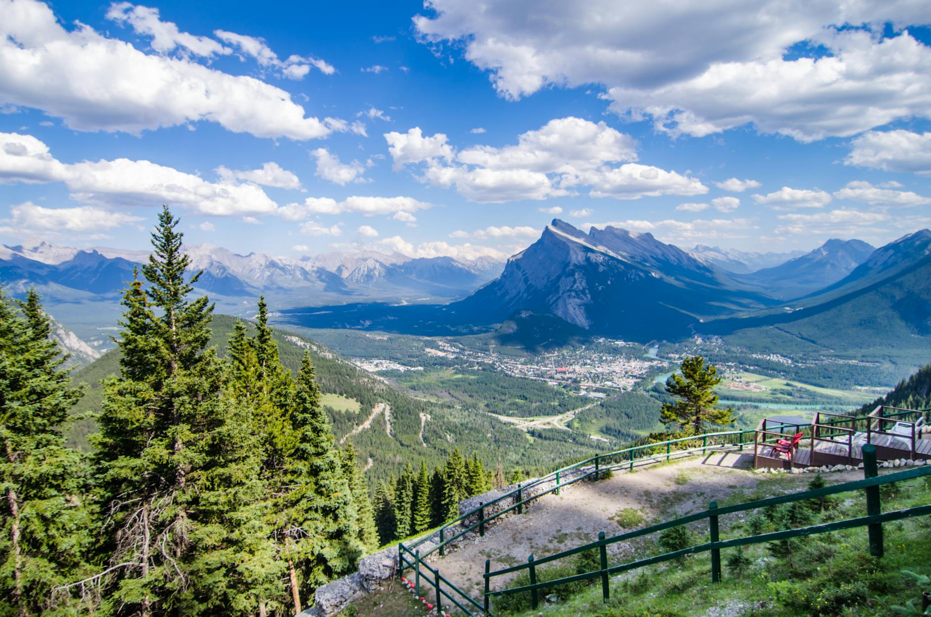 Scenic view from a railing overlooking mountains and a valley under a blue sky with clouds.