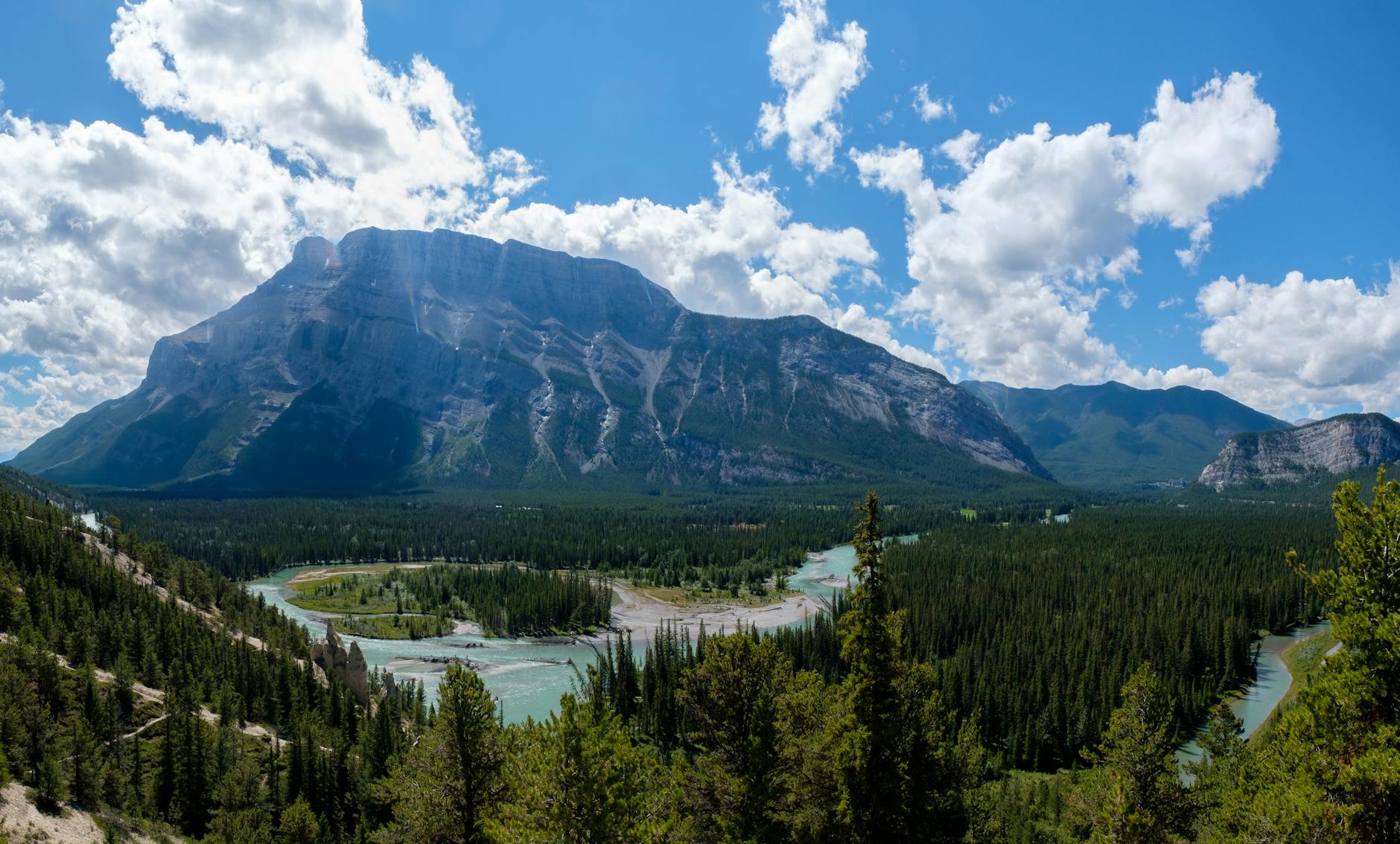 Majestic mountain range with lush forest in Banff National Park under a clear blue sky.