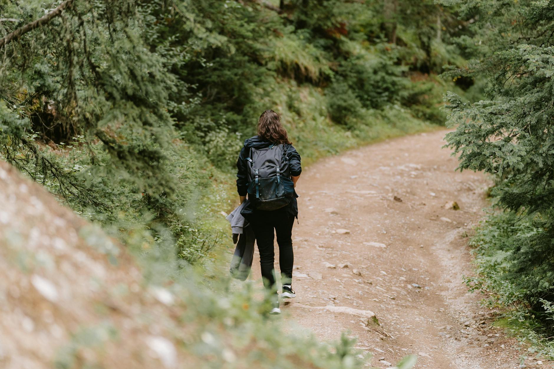 A woman hiking with a backpack on a scenic dirt road in Banff, surrounded by lush trees.