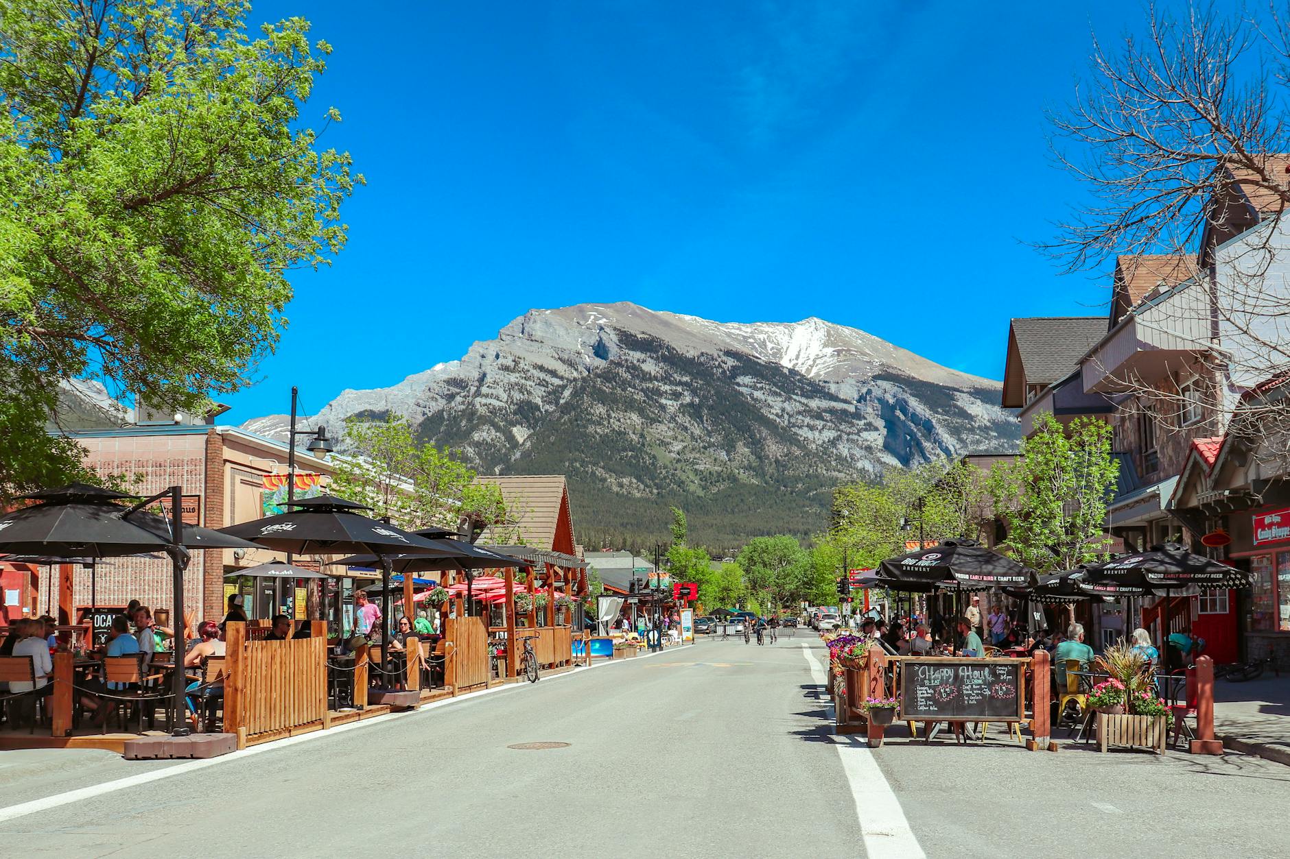 Lively street in Banff, Alberta with outdoor cafes and stunning mountain views, perfect for travel enthusiasts.