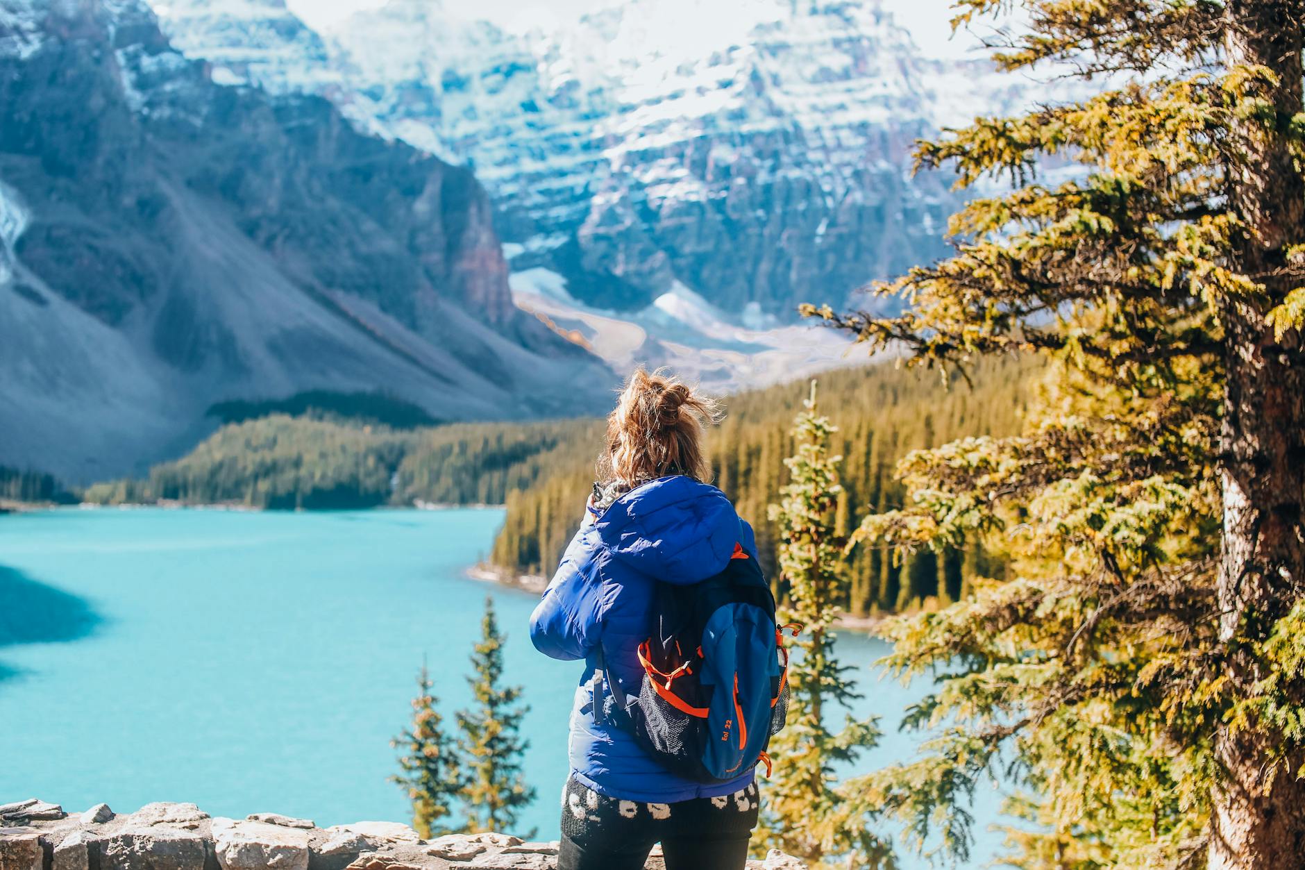 A woman in warm clothing overlooks a stunning mountain lake landscape in fall.