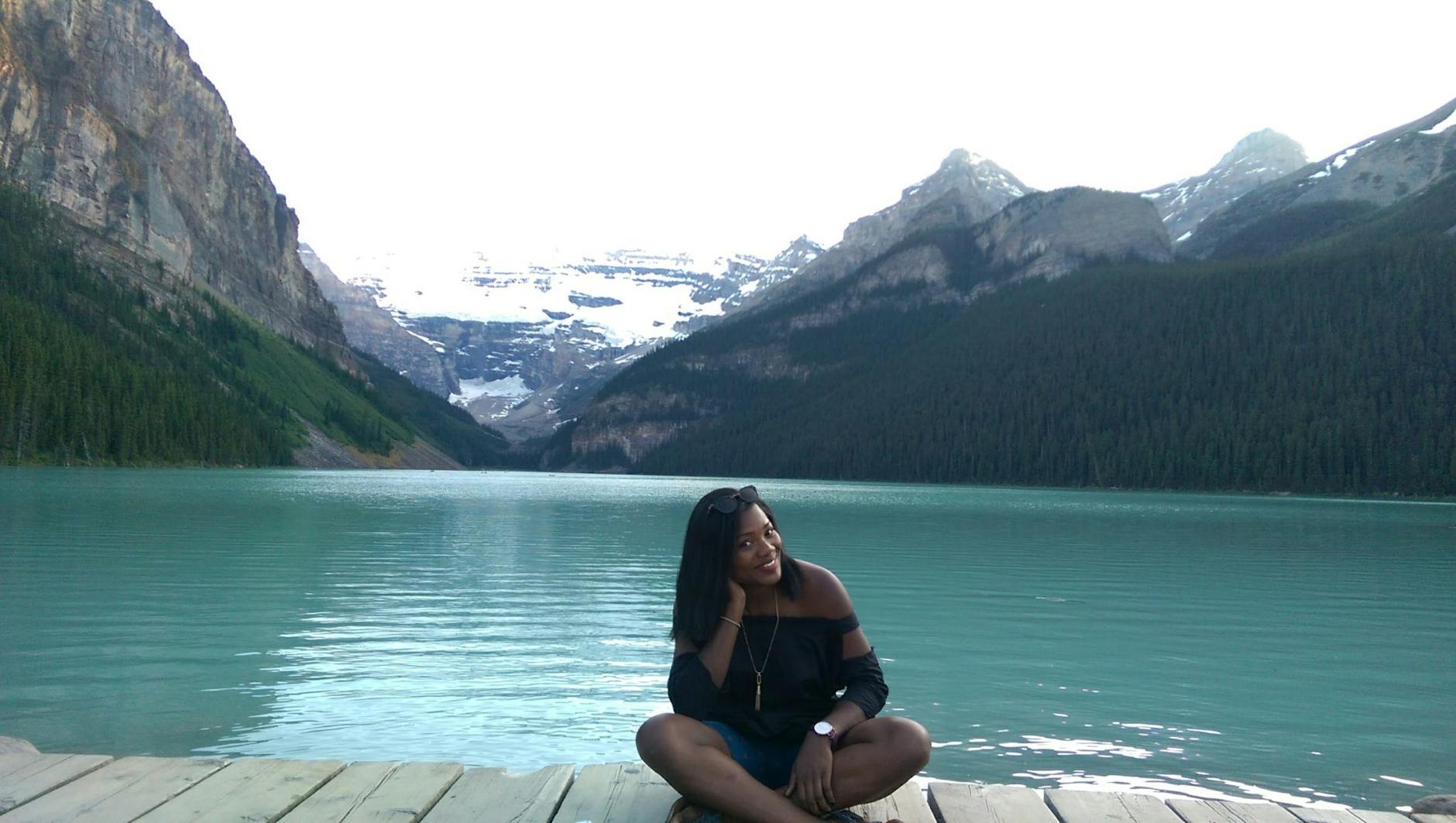 Woman sitting on a wooden deck beside Lake Louise with scenic mountain views.
