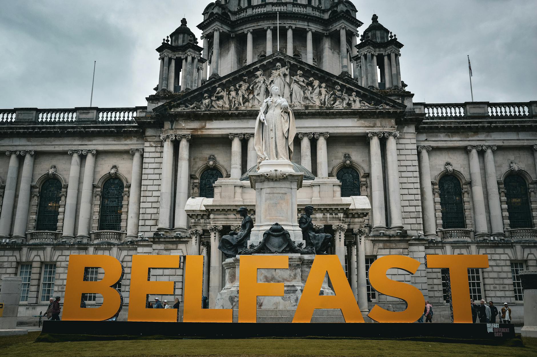View of the Belfast City Hall with striking statue and Belfast sign, showcasing historical architecture.