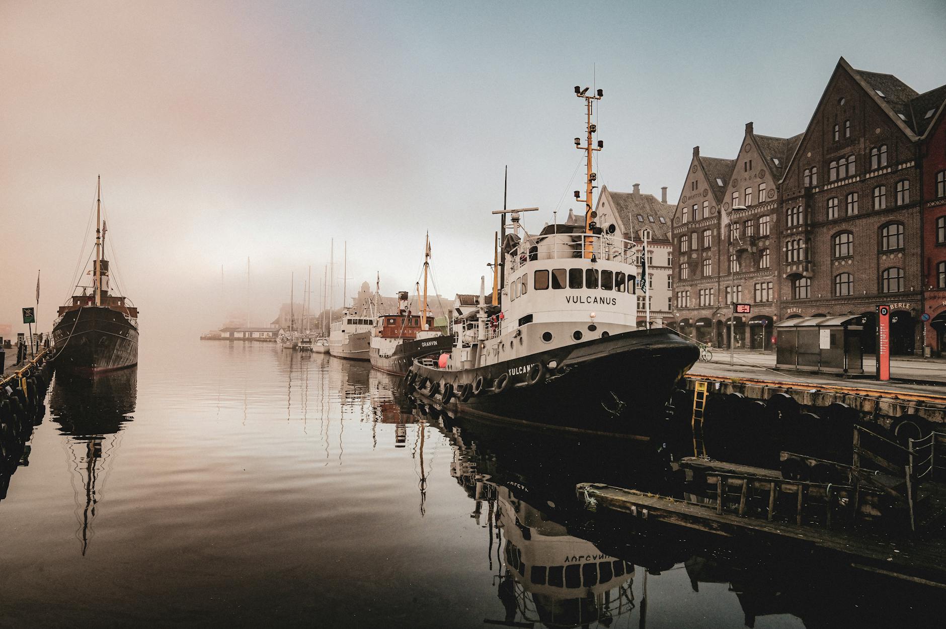Foggy Bergen harbor with boats for tourist food and break planning.