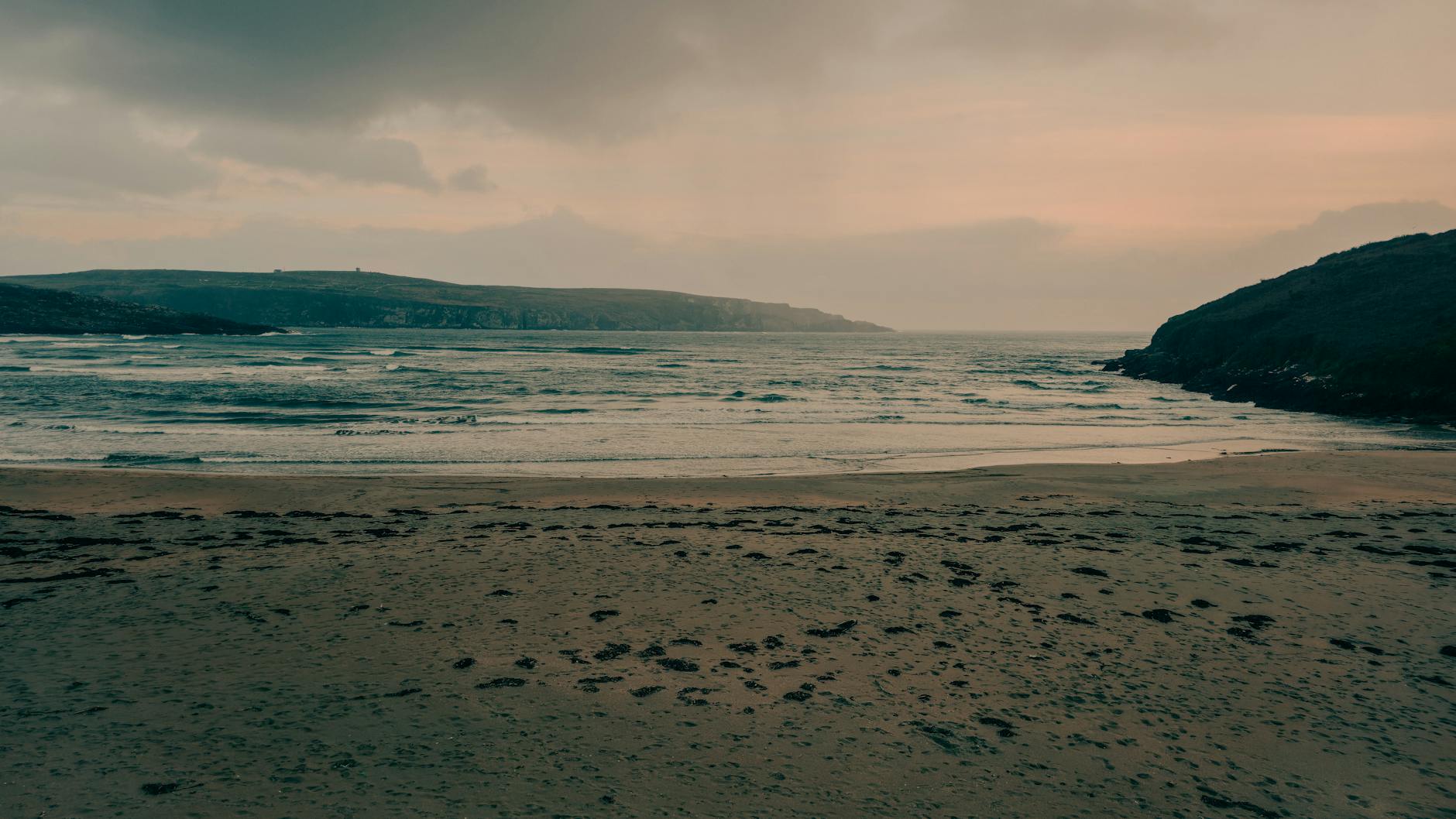 A tranquil beach scene at sunset in Cork, Ireland with gentle waves and a peaceful sky.