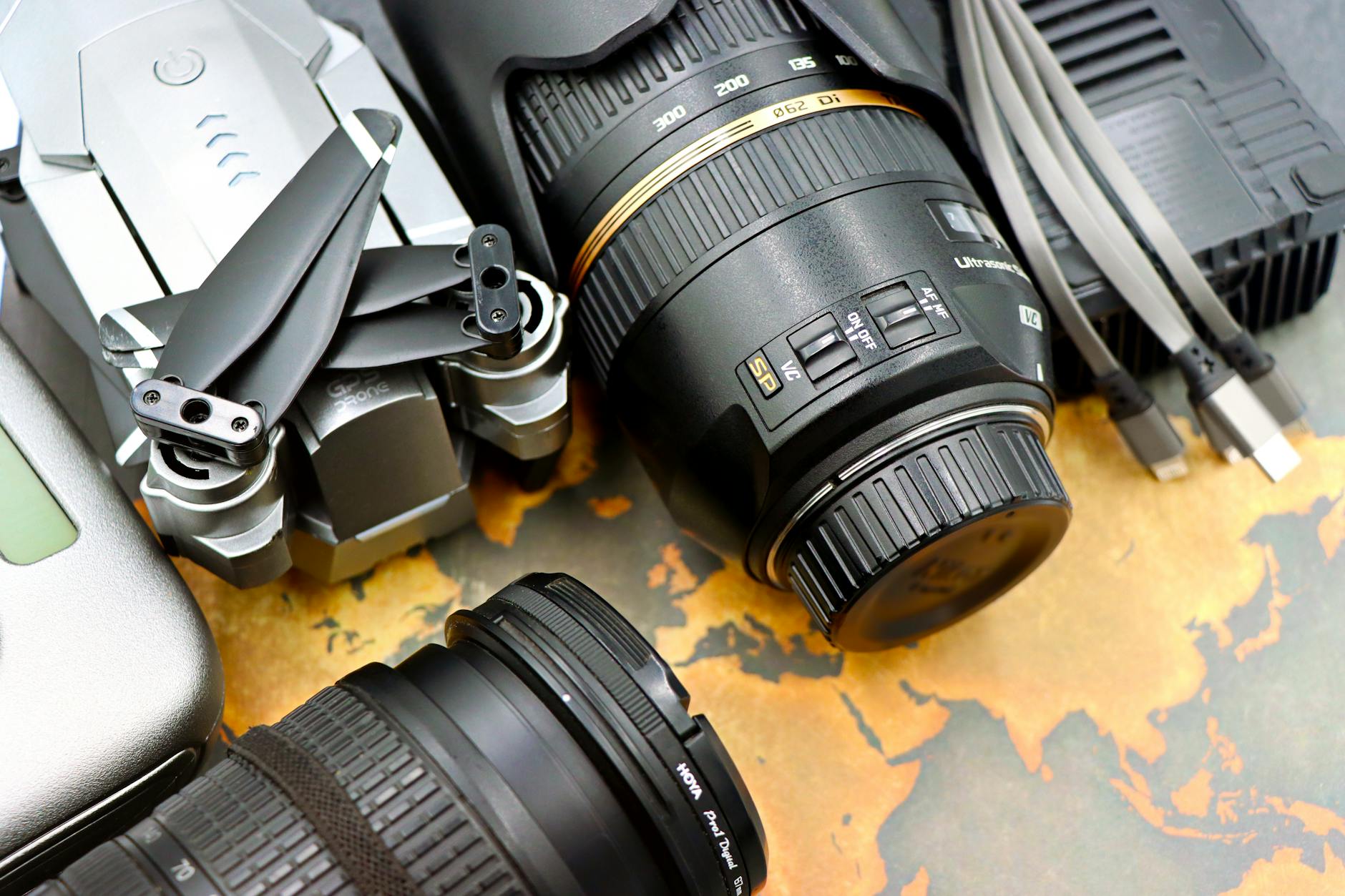 Top view of photography equipment including drone, camera lenses, and USB cables on a map background.