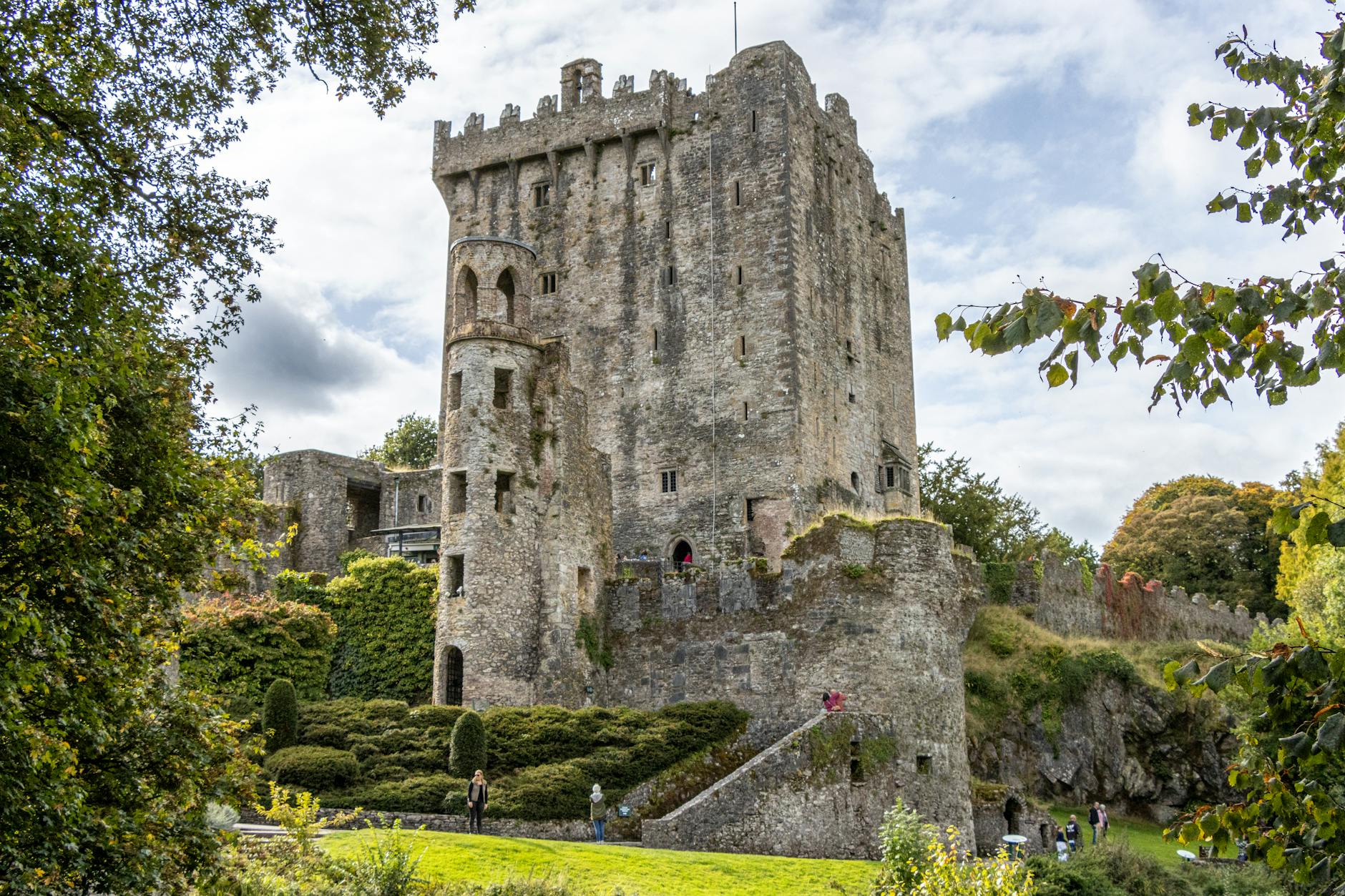 Historic Blarney Castle set against a backdrop of vibrant greenery and a partly cloudy sky.