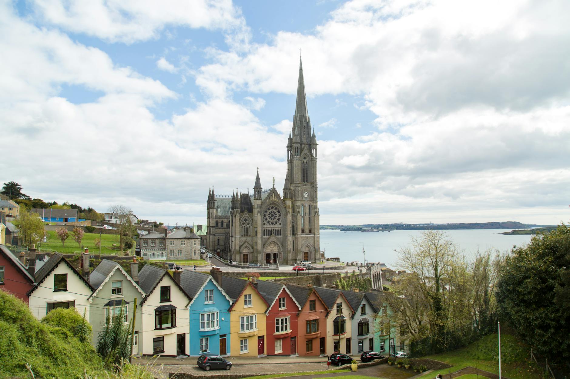 Picturesque St. Colman's Cathedral overlooking colorful houses and sea in Cobh, Ireland.
