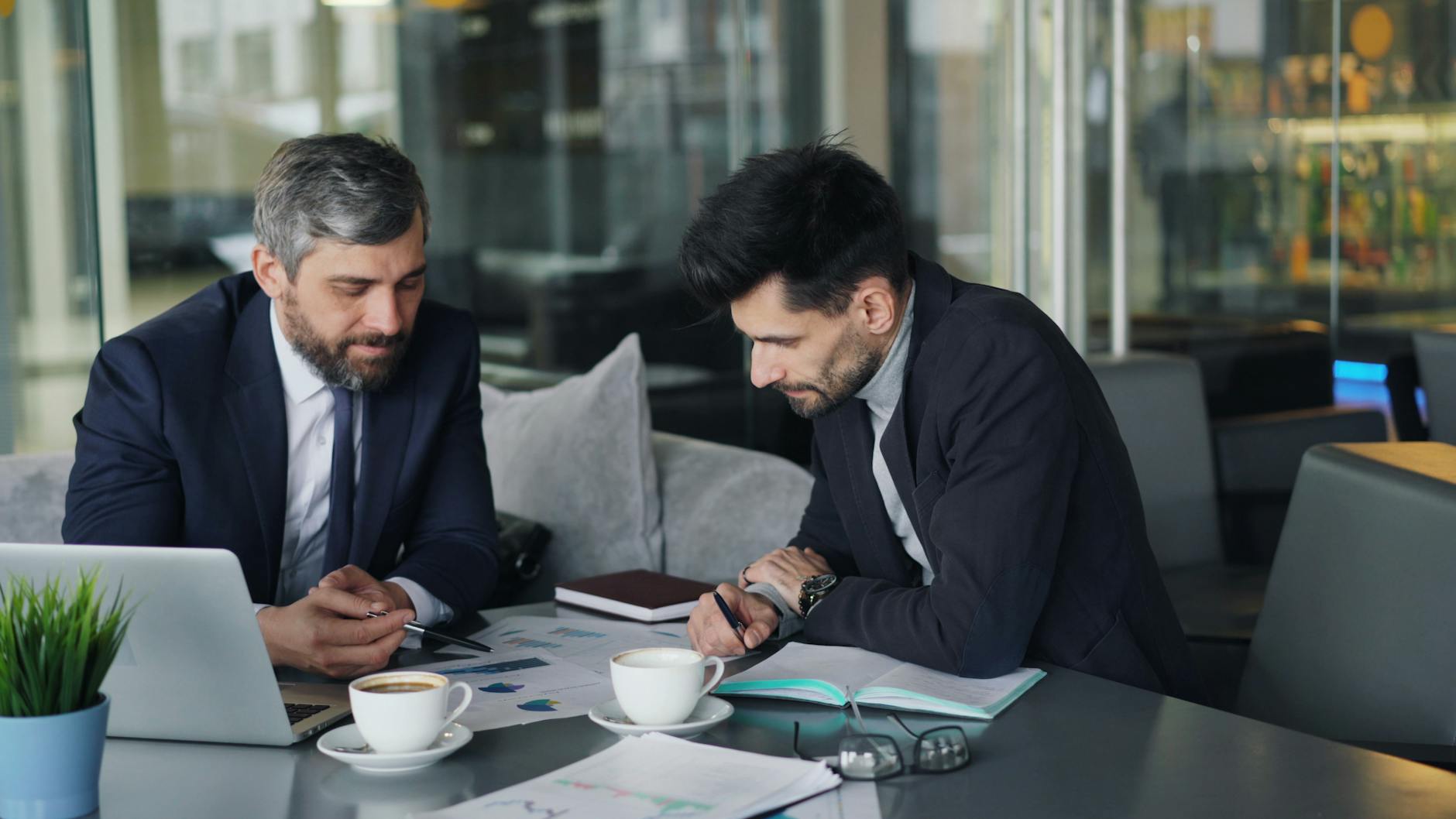 Two businessmen discussing charts over coffee at a cafe.