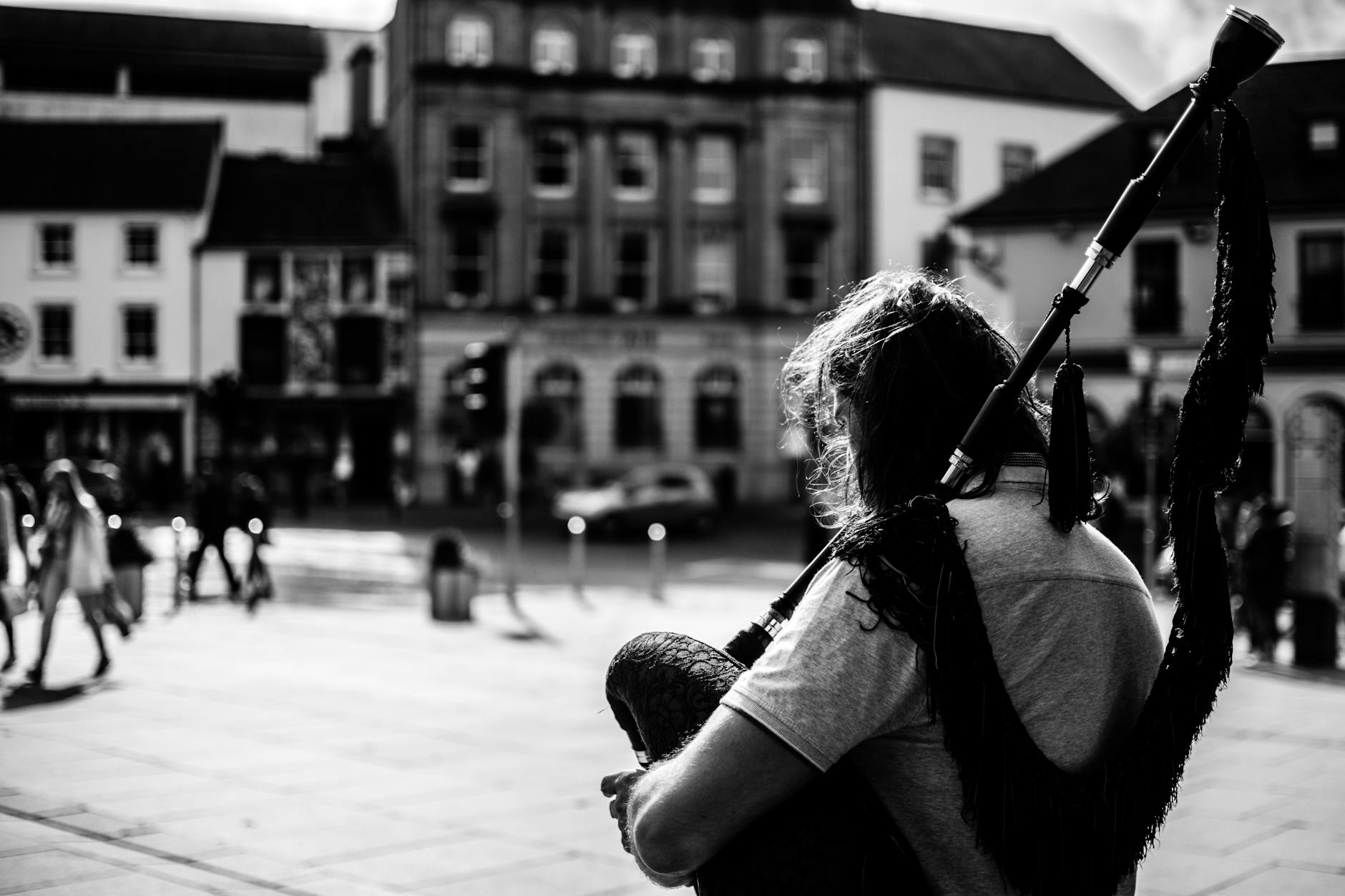 Black and white photo of a street musician playing bagpipes in an Irish city.