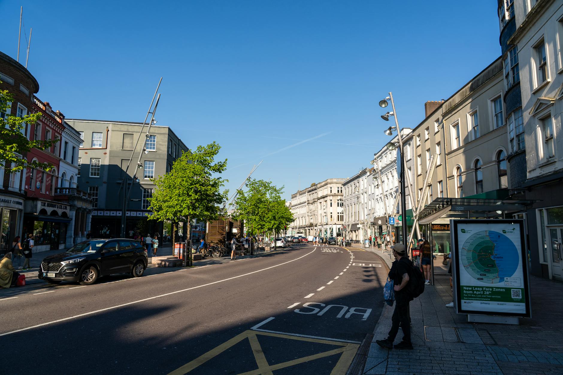 Sunny street view in Cork, Ireland, showcasing vibrant architecture and daily urban life.