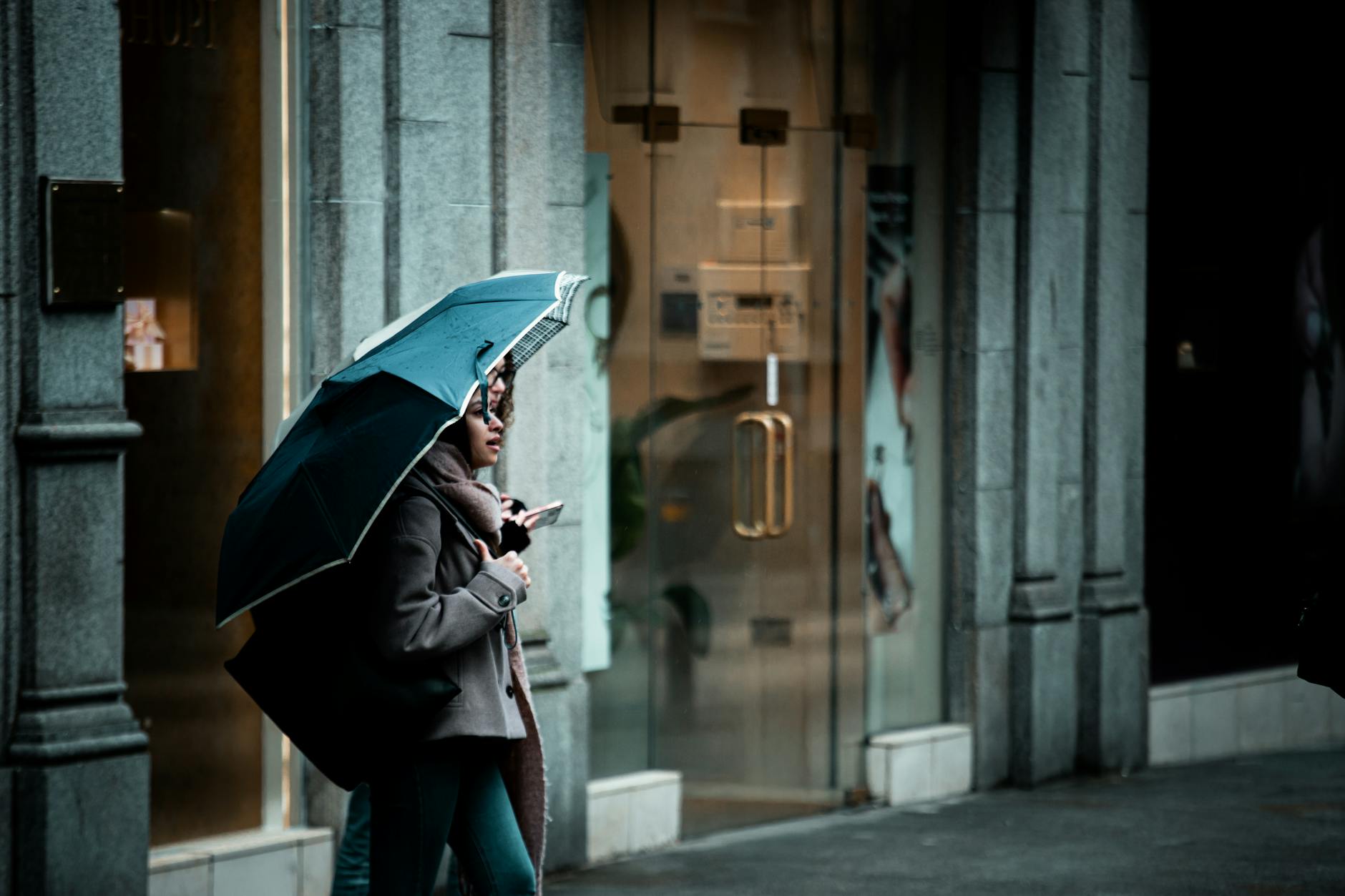 A woman walks with an umbrella near a shopfront on a rainy day in Ireland, capturing urban life.