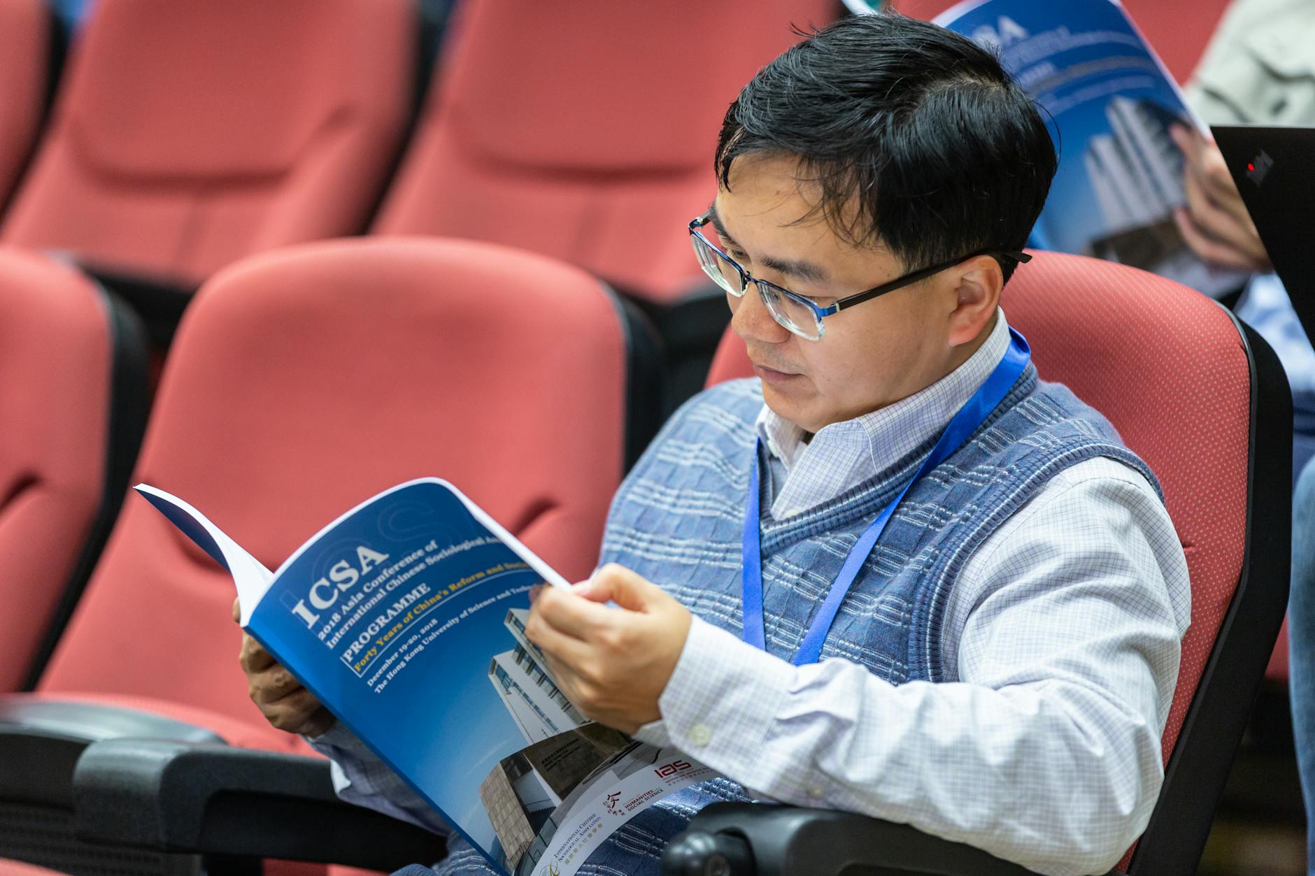 Conference attendee reading a program in an auditorium for Delhi academic scheduling.